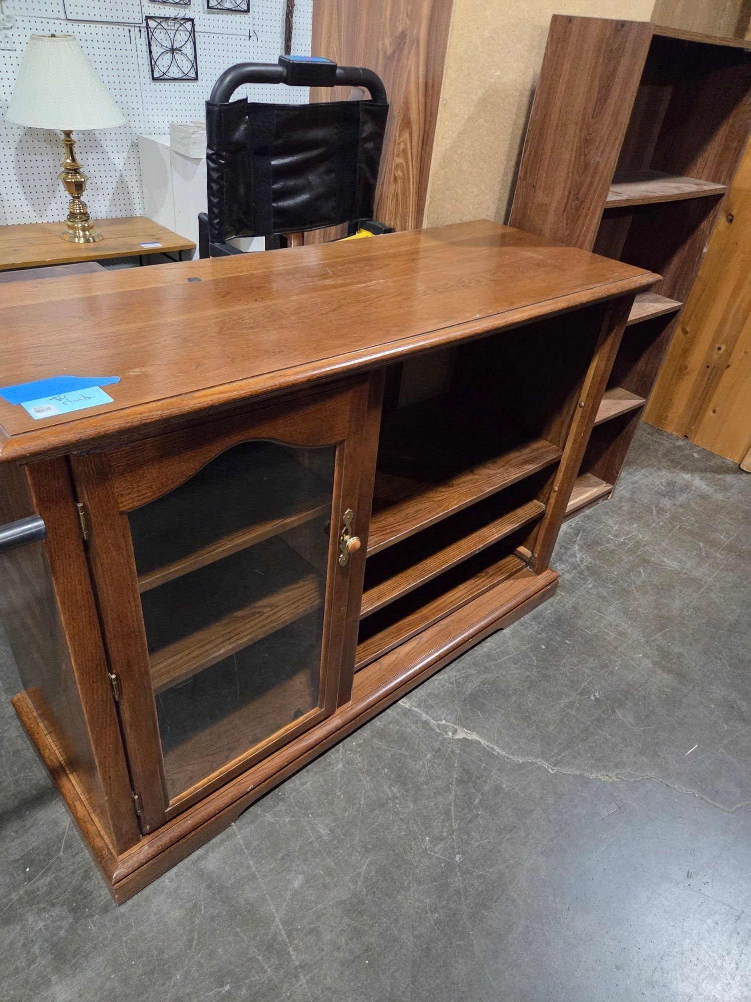 Wooden office credenza with sliding glass doors and open shelves on a concrete floor in a showroom