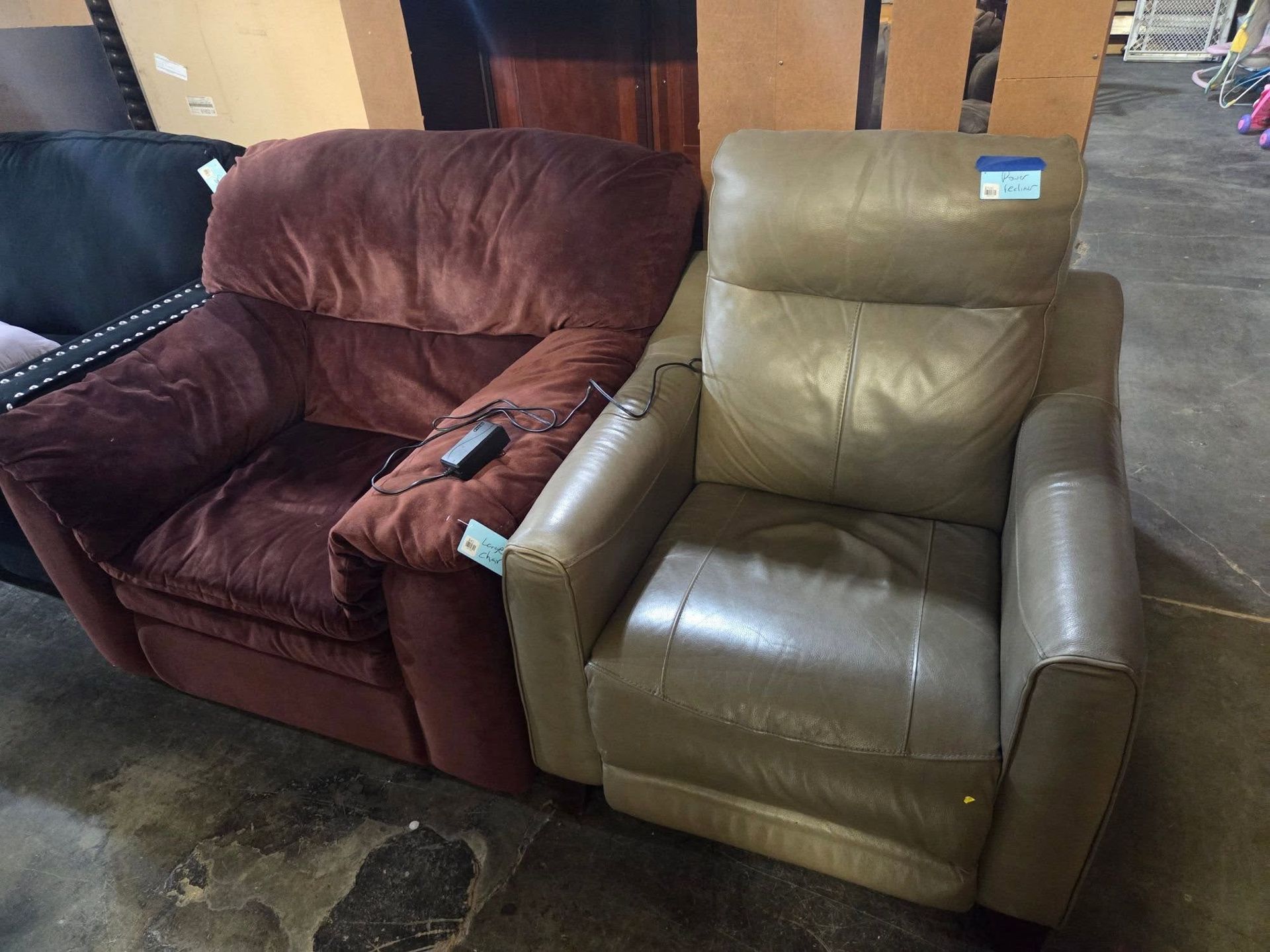 Two recliner chairs in a furniture store, one burgundy and one tan, both slightly worn.