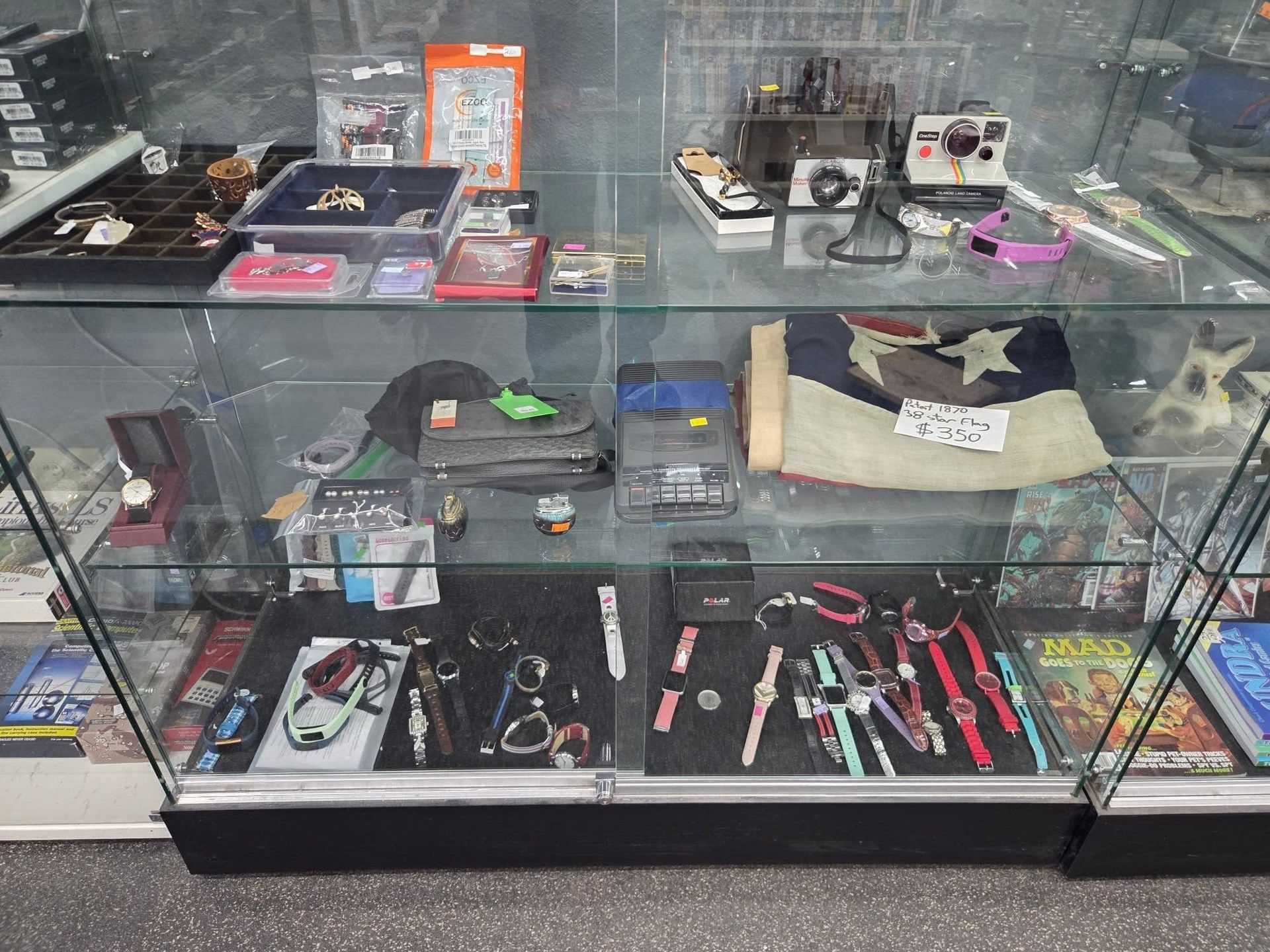 Glass display case with assorted knives, tools, and small collectibles on shelves.