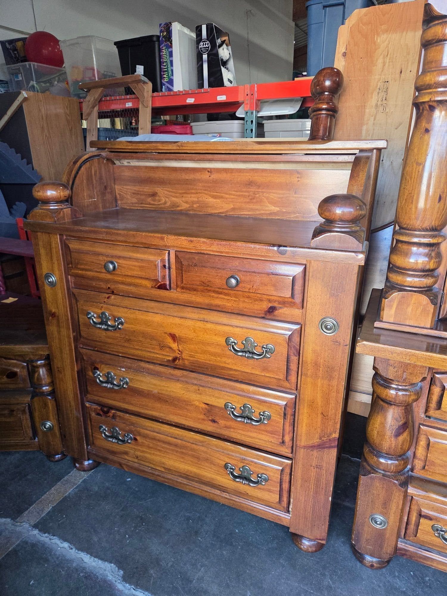 Wooden antique dresser with four drawers and brass handles in a storage room, surrounded by furniture