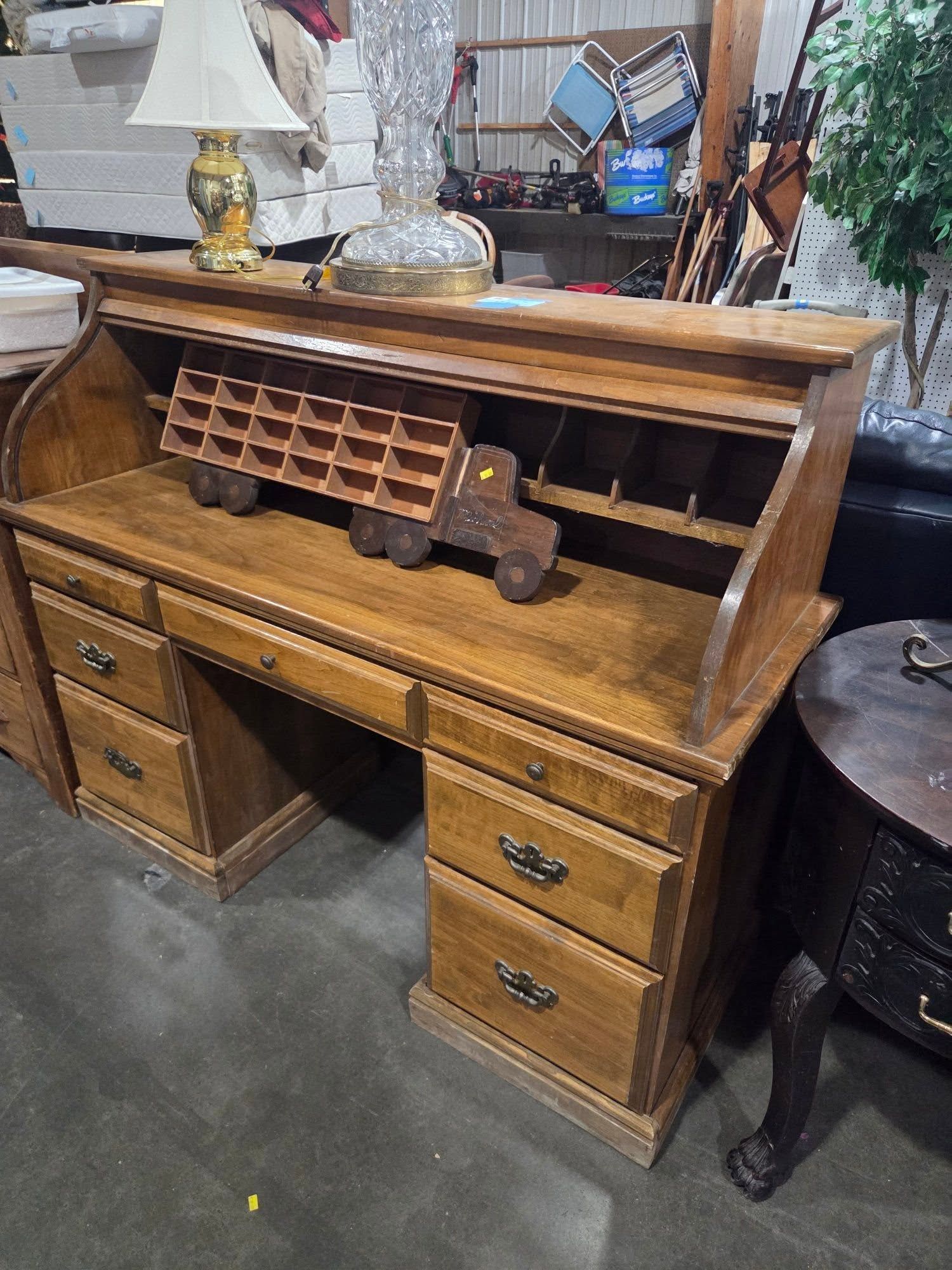 Antique wooden roll-top desk with drawers, small cubbies, and a brass lamp on top in a workshop-like space