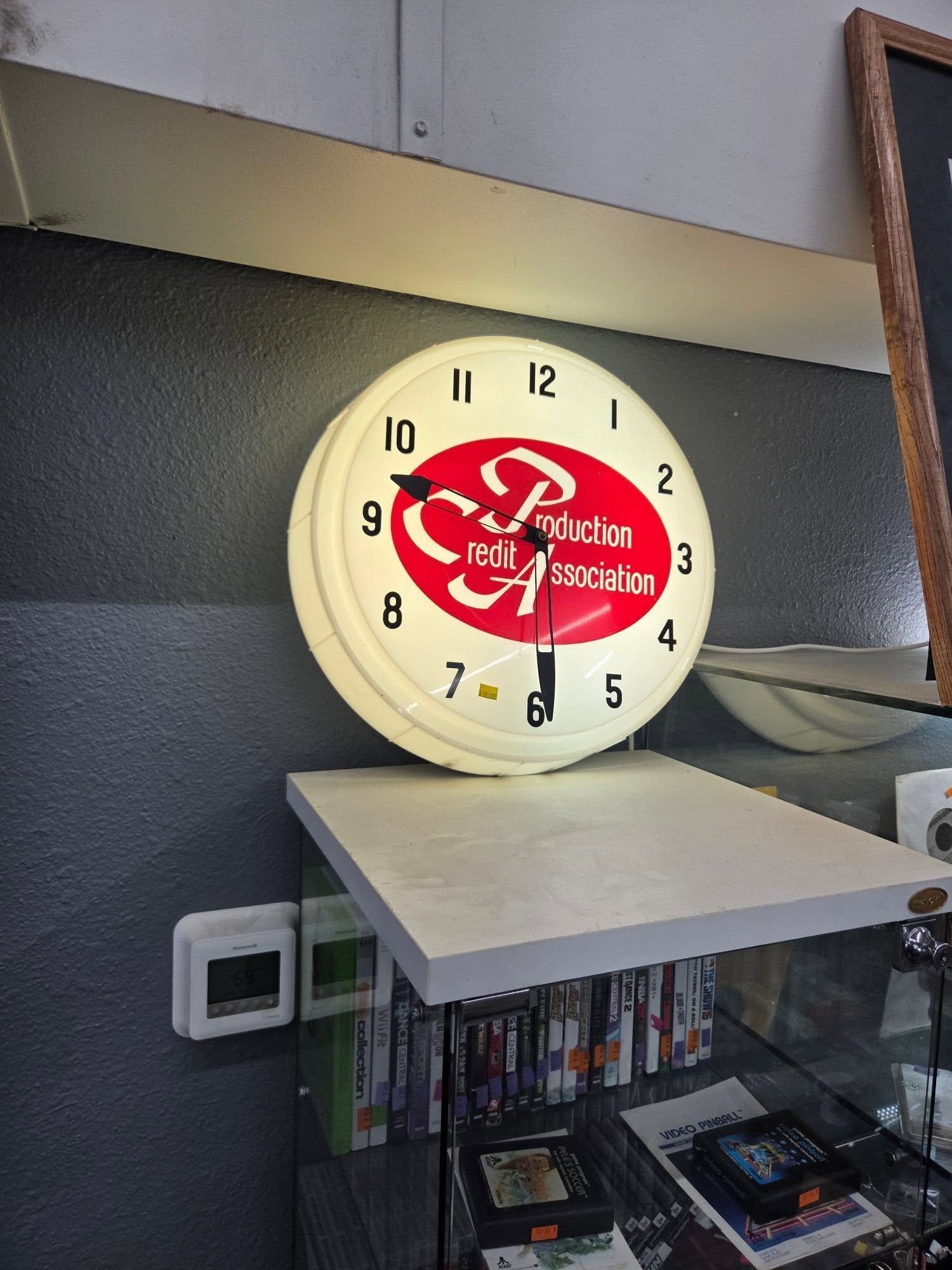 Round wall clock with a red center sitting on a shelf above books in an office-like space