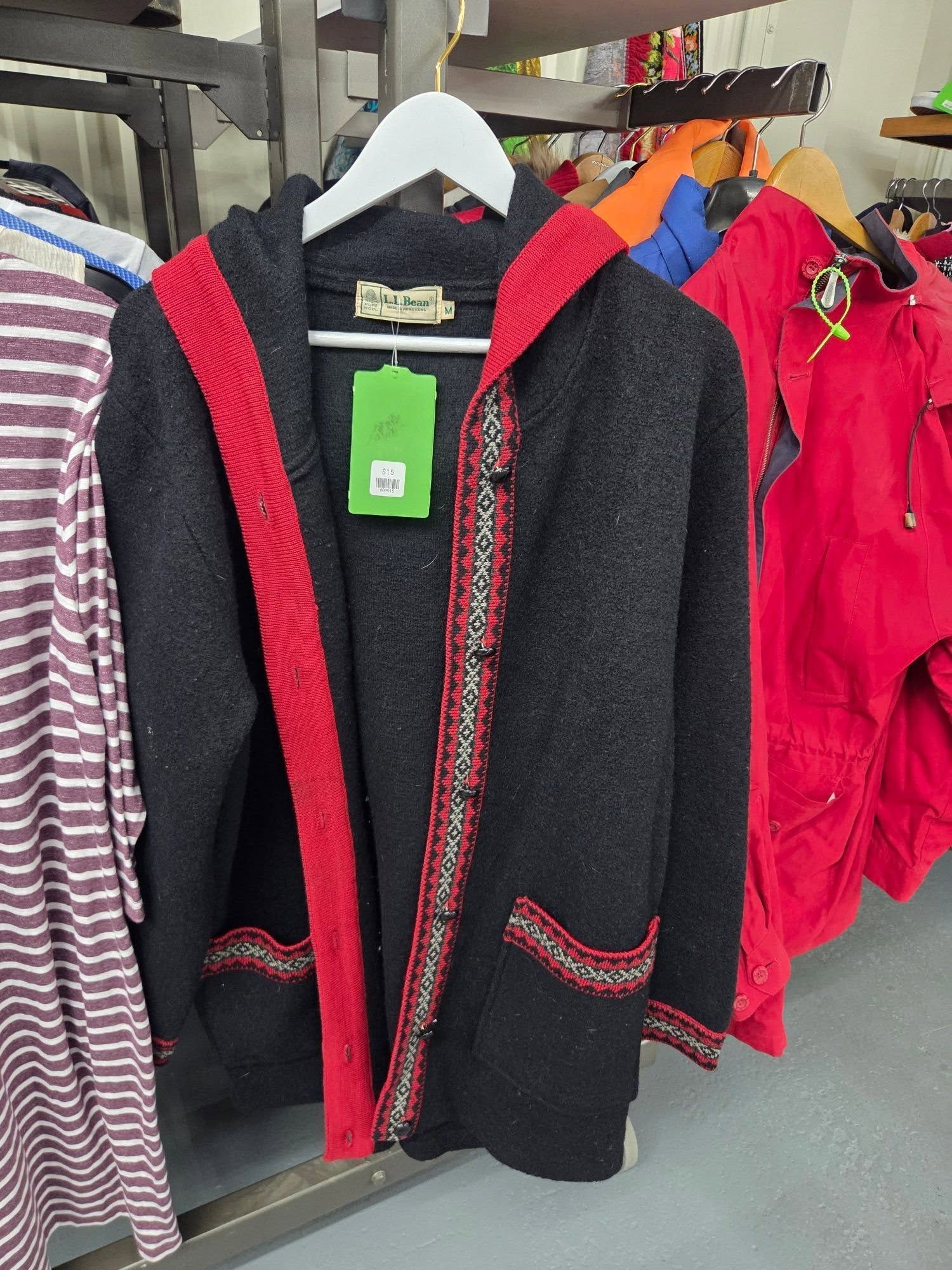 Black-and-red hooded sweater on a hanger in a clothing store, with striped shirts and bright jackets nearby