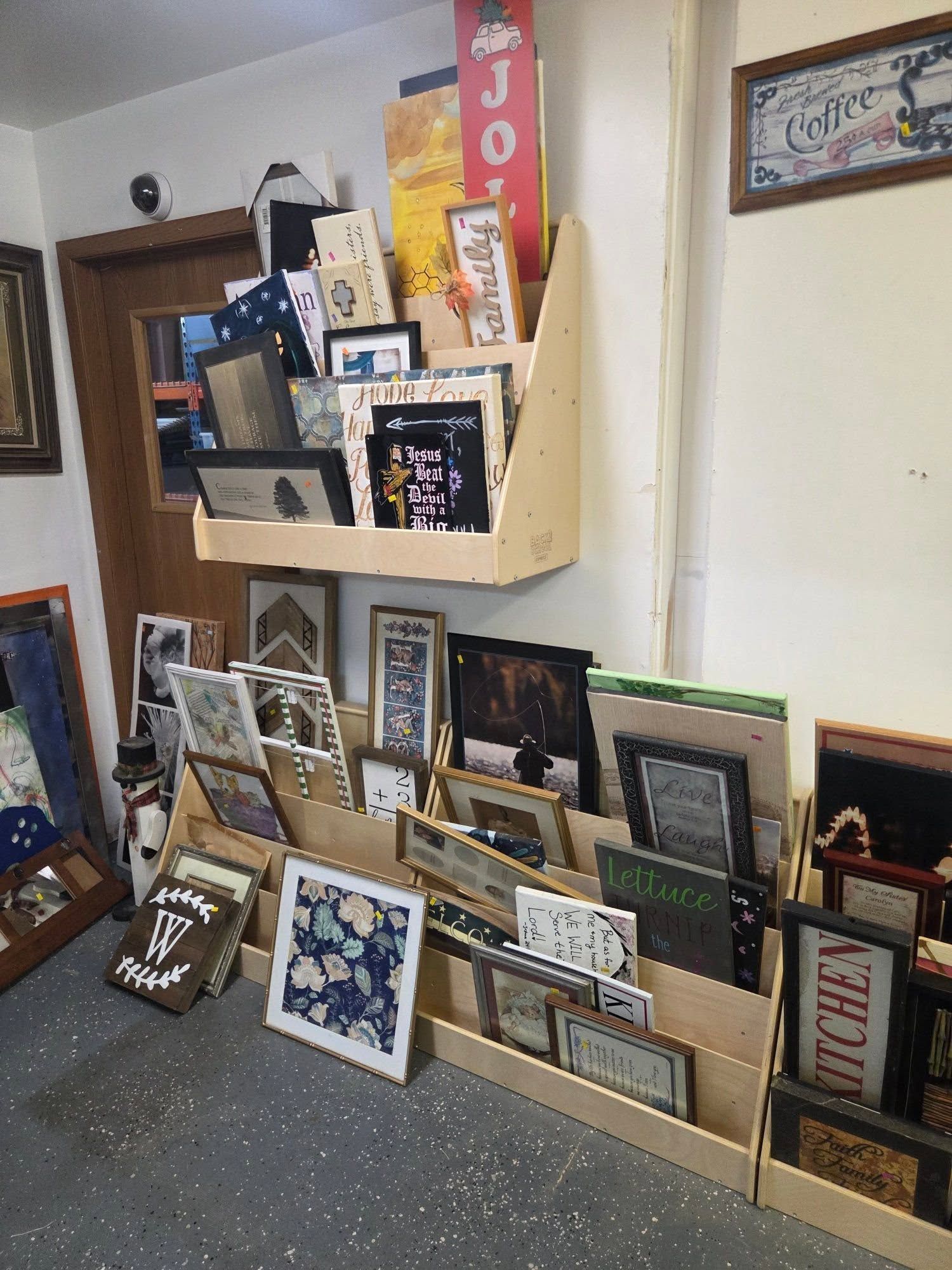 Framed artwork and signs displayed in a shop or gallery on shelves and the floor