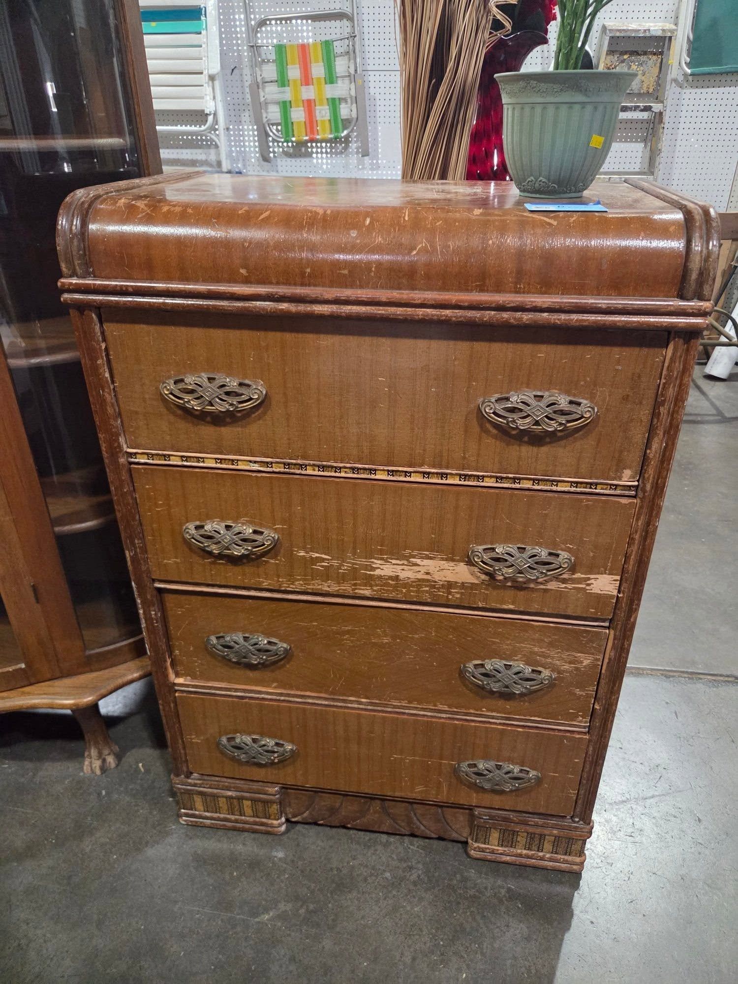 Brown wooden four-drawer dresser with ornate handles in a furniture store.