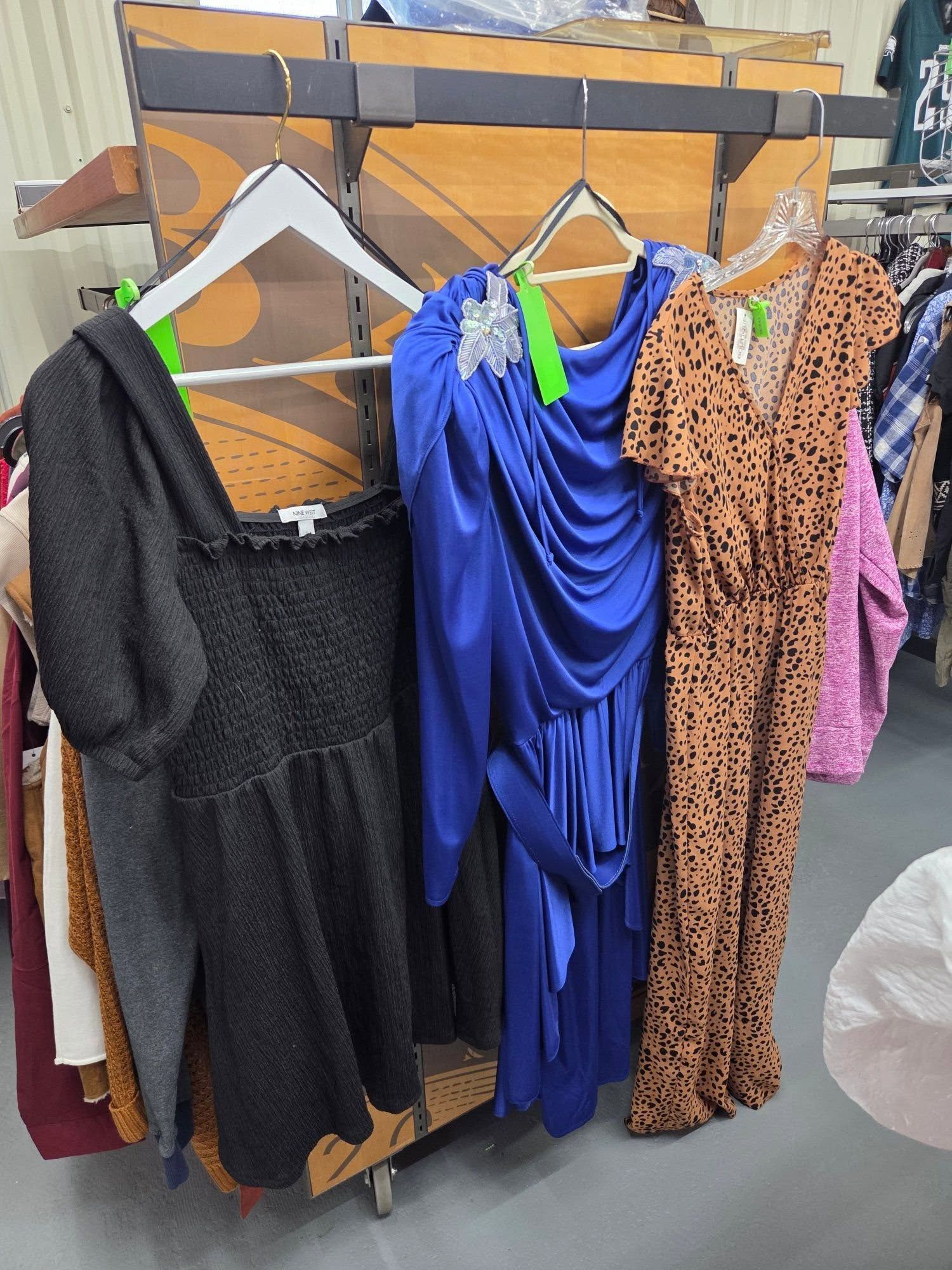 Three dresses on hangers: black, royal blue, and tan leopard print, displayed on a wooden rack.