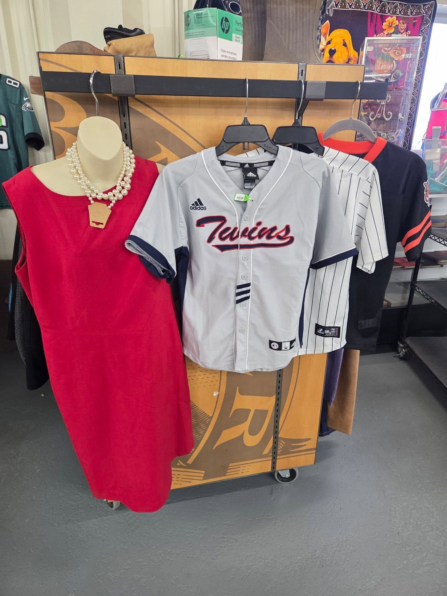 Clothing rack with a red dress and Minnesota Twins jerseys on mannequins in a shop.