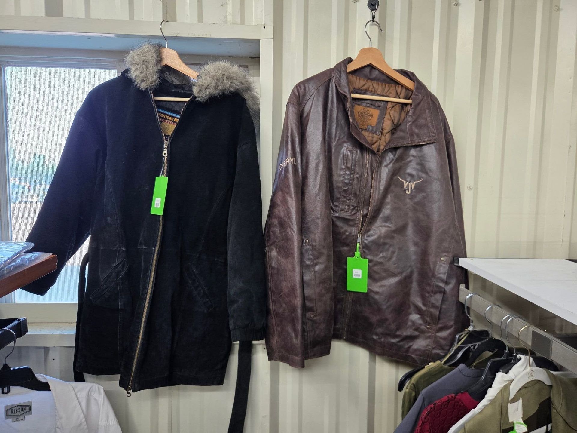 Two coats on hangers, one dark navy with fur hood and one brown leather jacket, in a store display