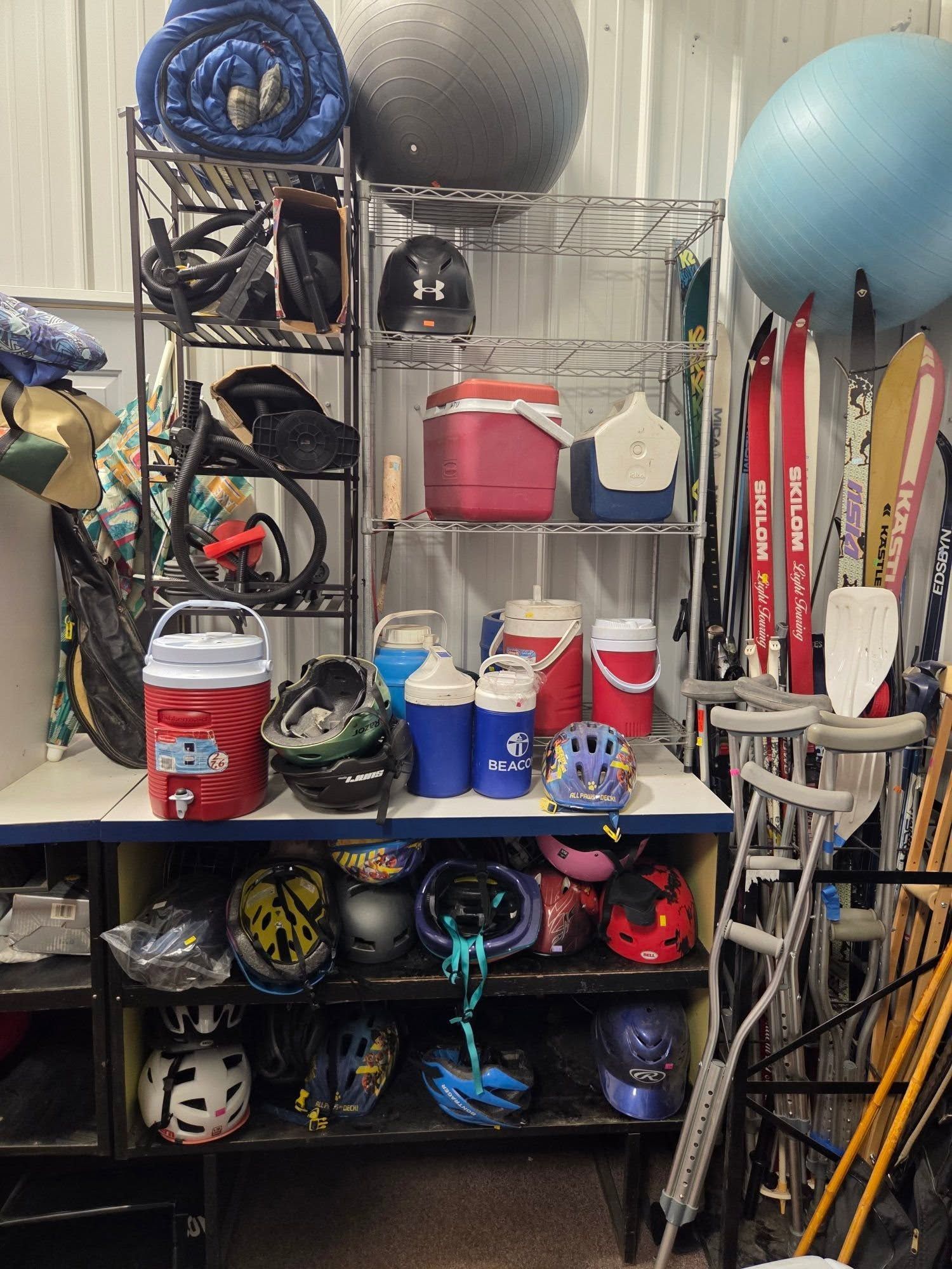 Cluttered garage shelf with helmets, buckets, skis, balls, and sports gear stacked tightly