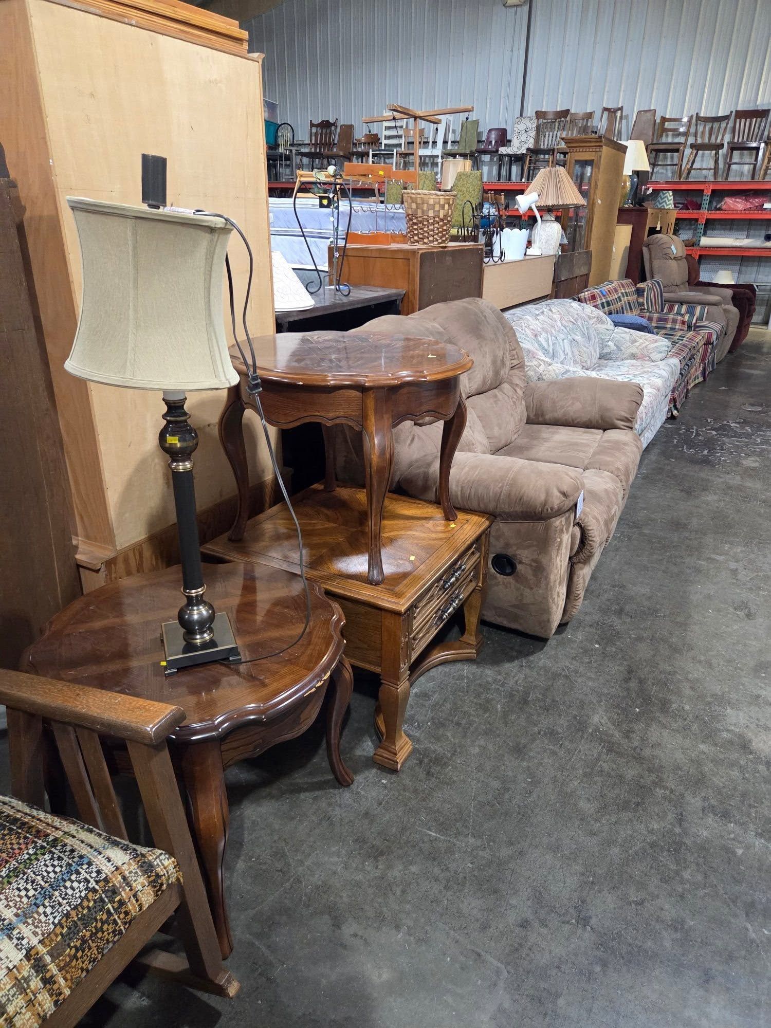 Furniture store aisle with sofas, side tables, and lamps displayed on carpeted floor.