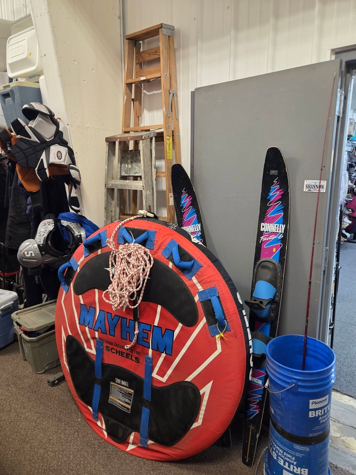 Red and blue inflatable towable tube leaning in a storage room beside skis and buckets