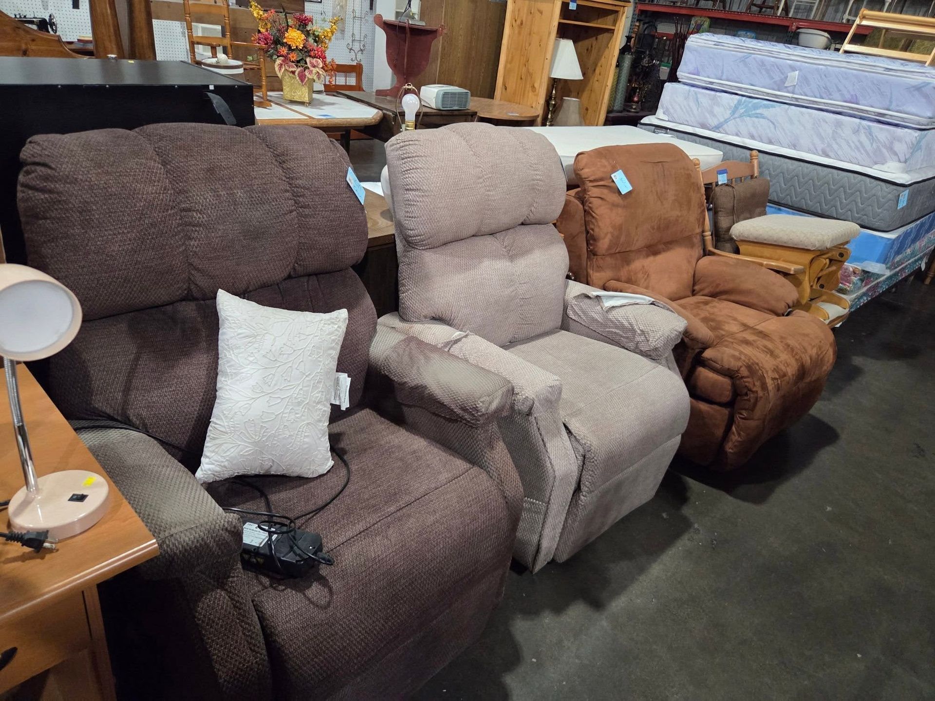 Three reclining chairs in brown, beige, and tan displayed in a furniture store warehouse.