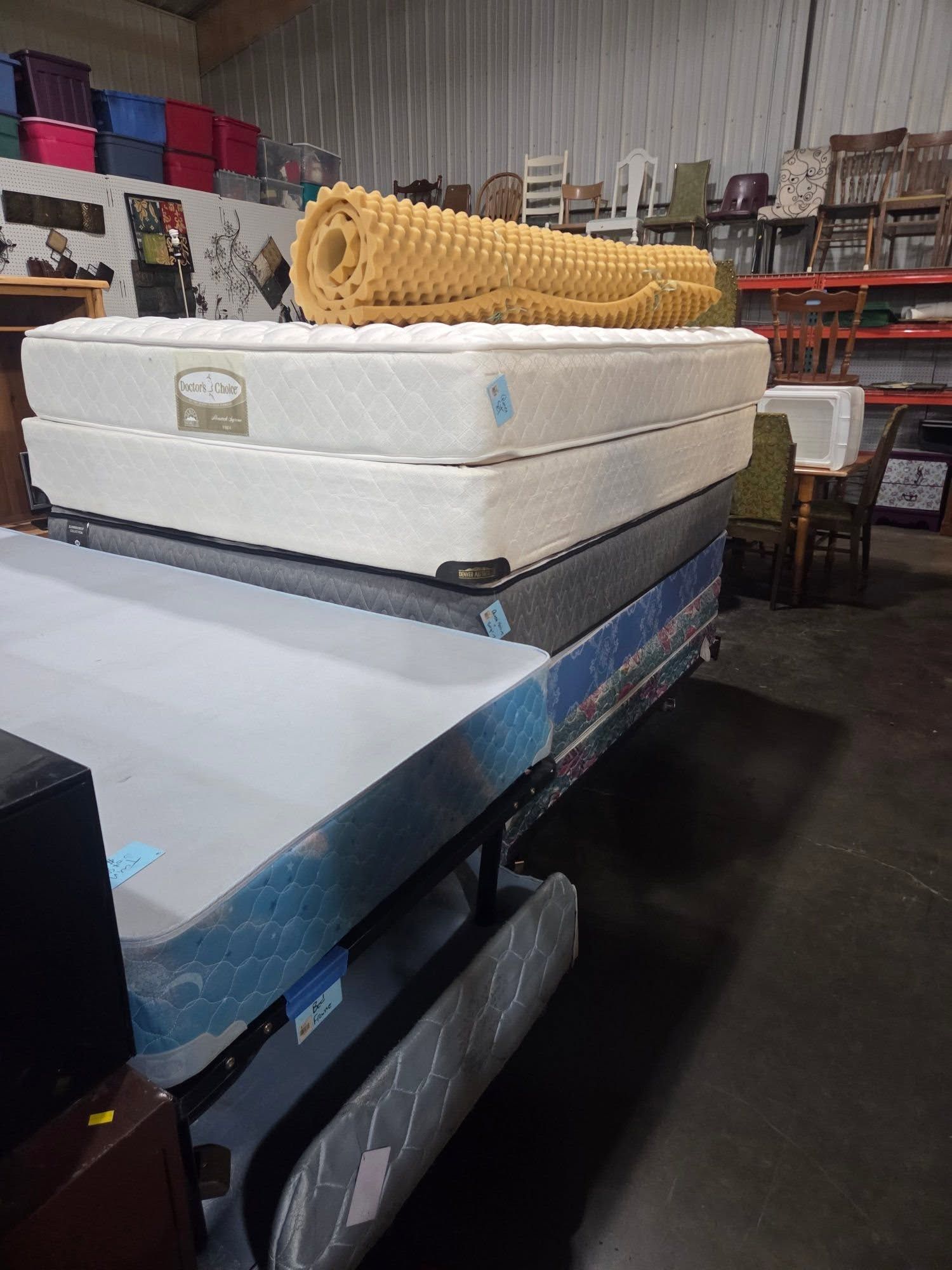 Stacked foam and cushions on a pallet in a warehouse aisle, with shelves and storage racks behind.