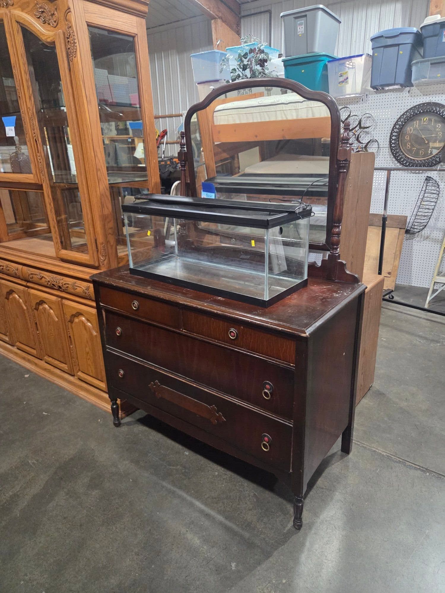 Antique wooden dresser with glass display case in an antique shop, surrounded by other furniture.
