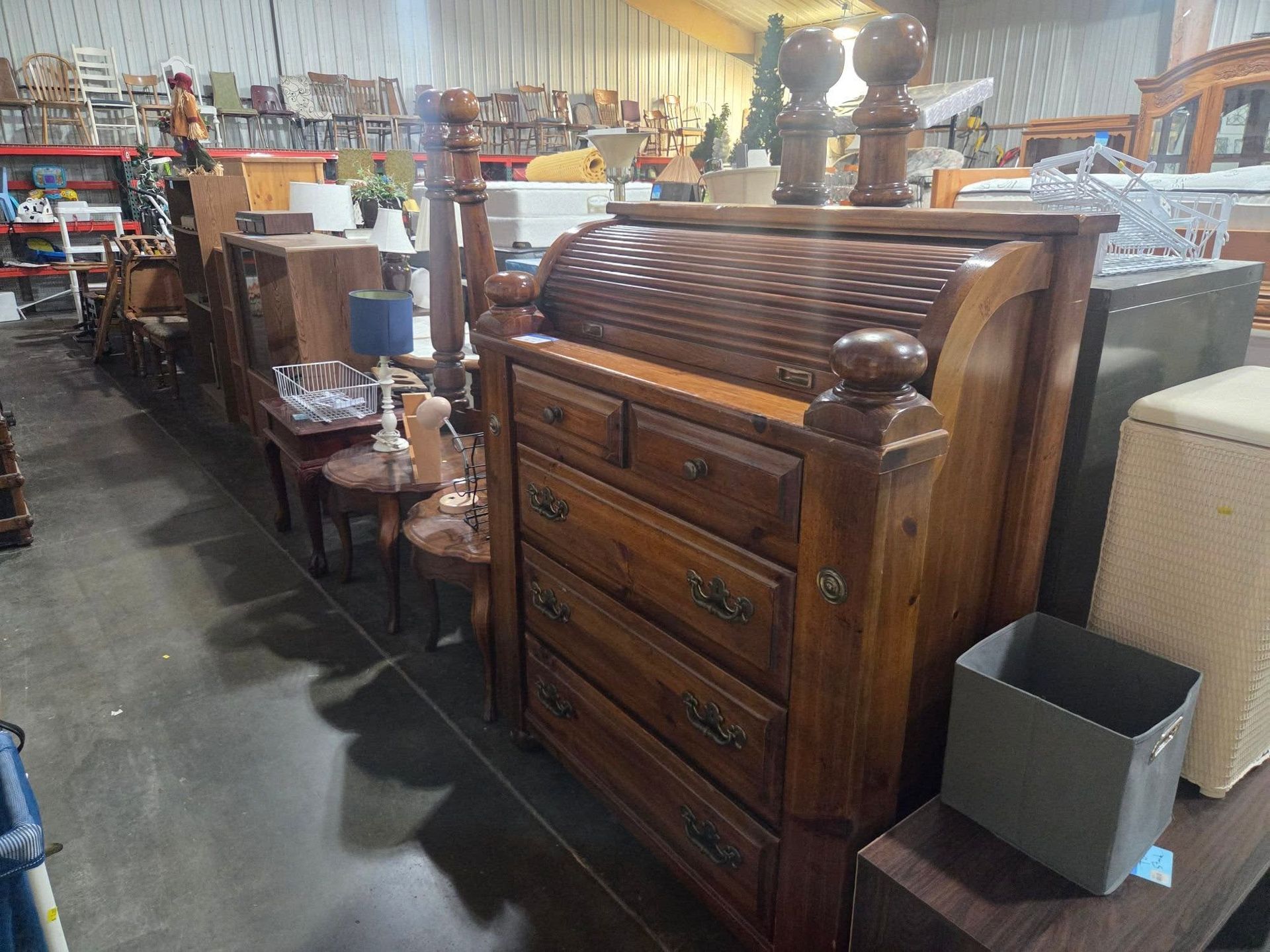 Large wooden dresser and antique furniture displayed in a warehouse-style store aisle.