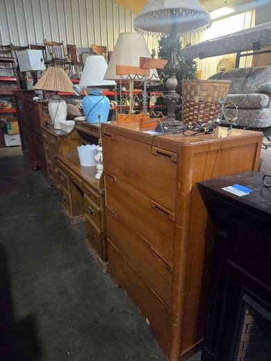 Antique wooden furniture display in a shop, with lamps, decor, and a carved cabinet in the foreground
