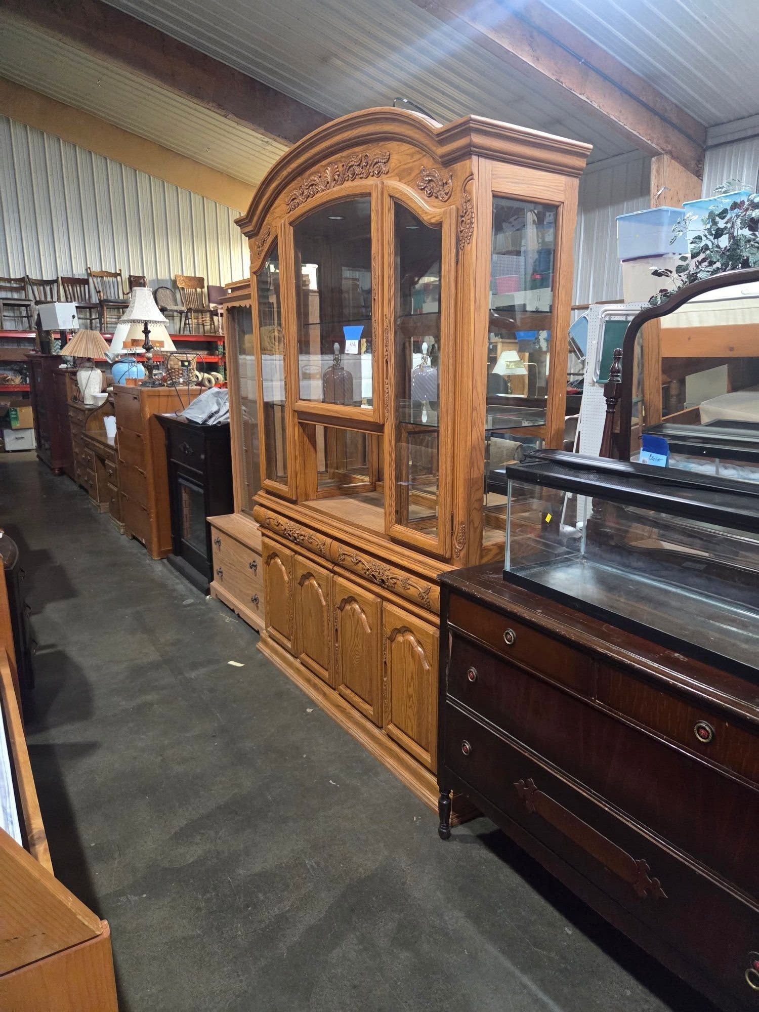 Wooden china cabinet with glass doors in a furniture showroom, alongside other antique dressers.