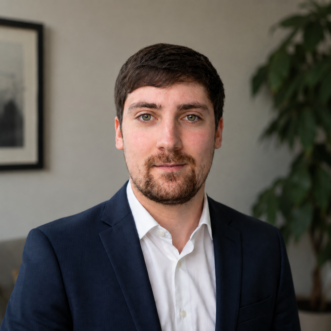Image of Luke Statham in black tuxedo and bow tie, brown hair, slight beard, smiling, bookshelves in background.