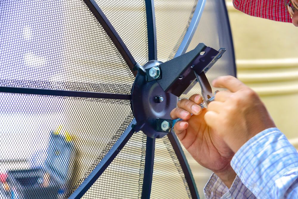 A Man Is Fixing a Satellite Dish with A Wrench — BTV Antenna & Data in Coral Cove, QLD