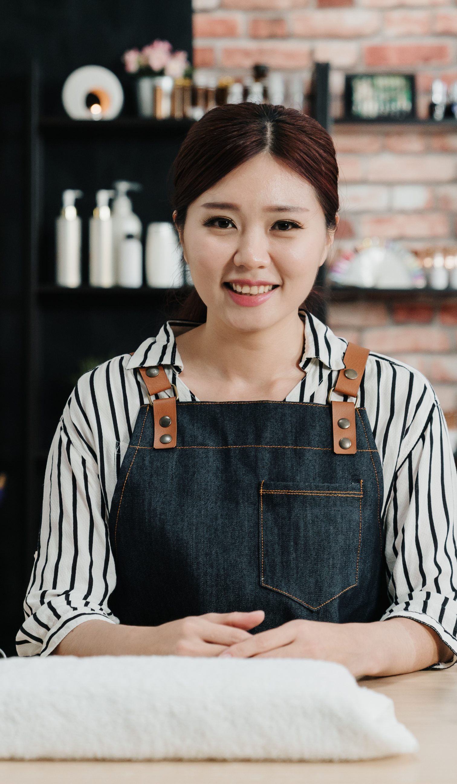 a woman in an apron is sitting at a table in a salon .