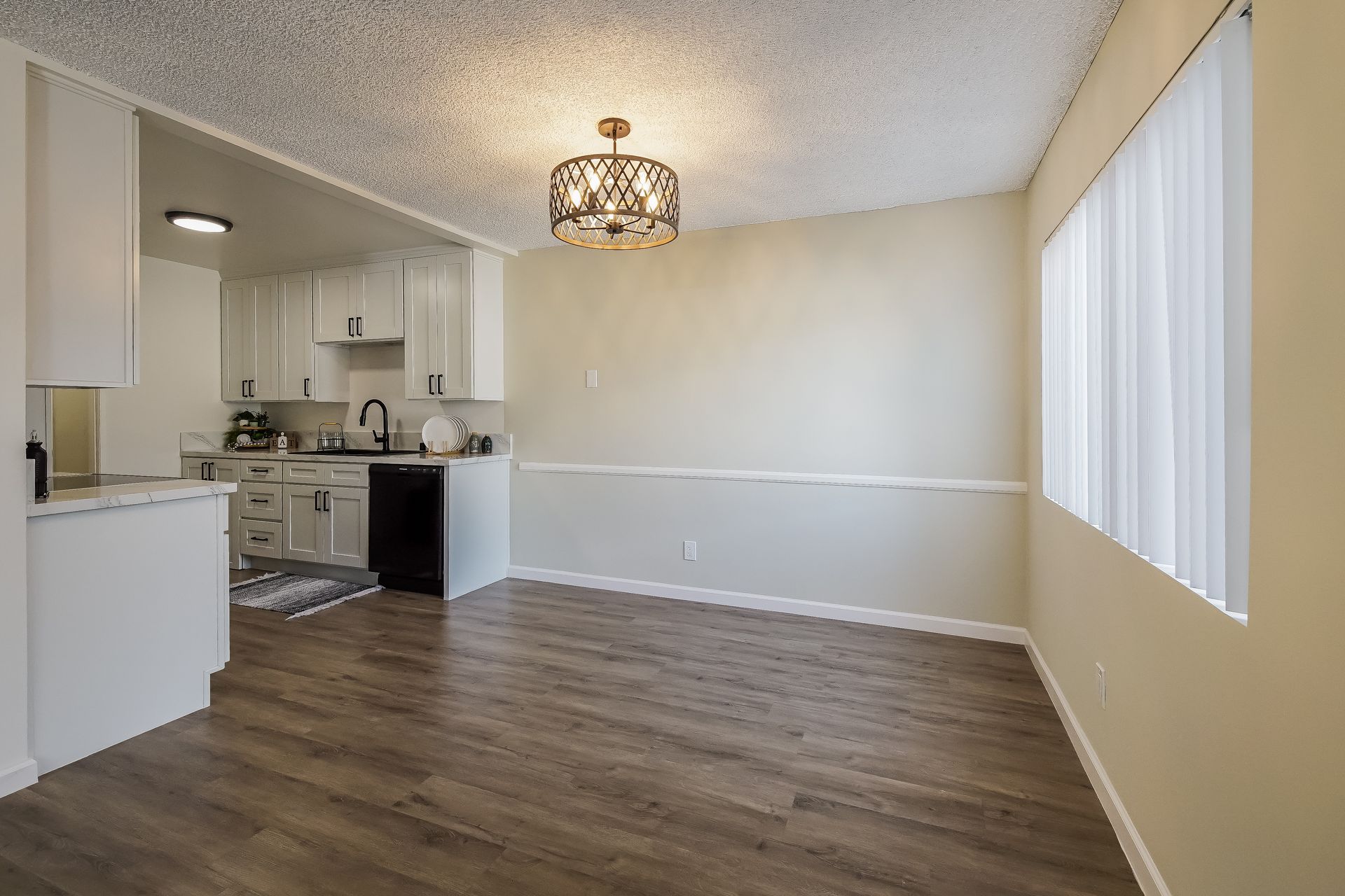 A living room with hardwood floors and a kitchen in the background.