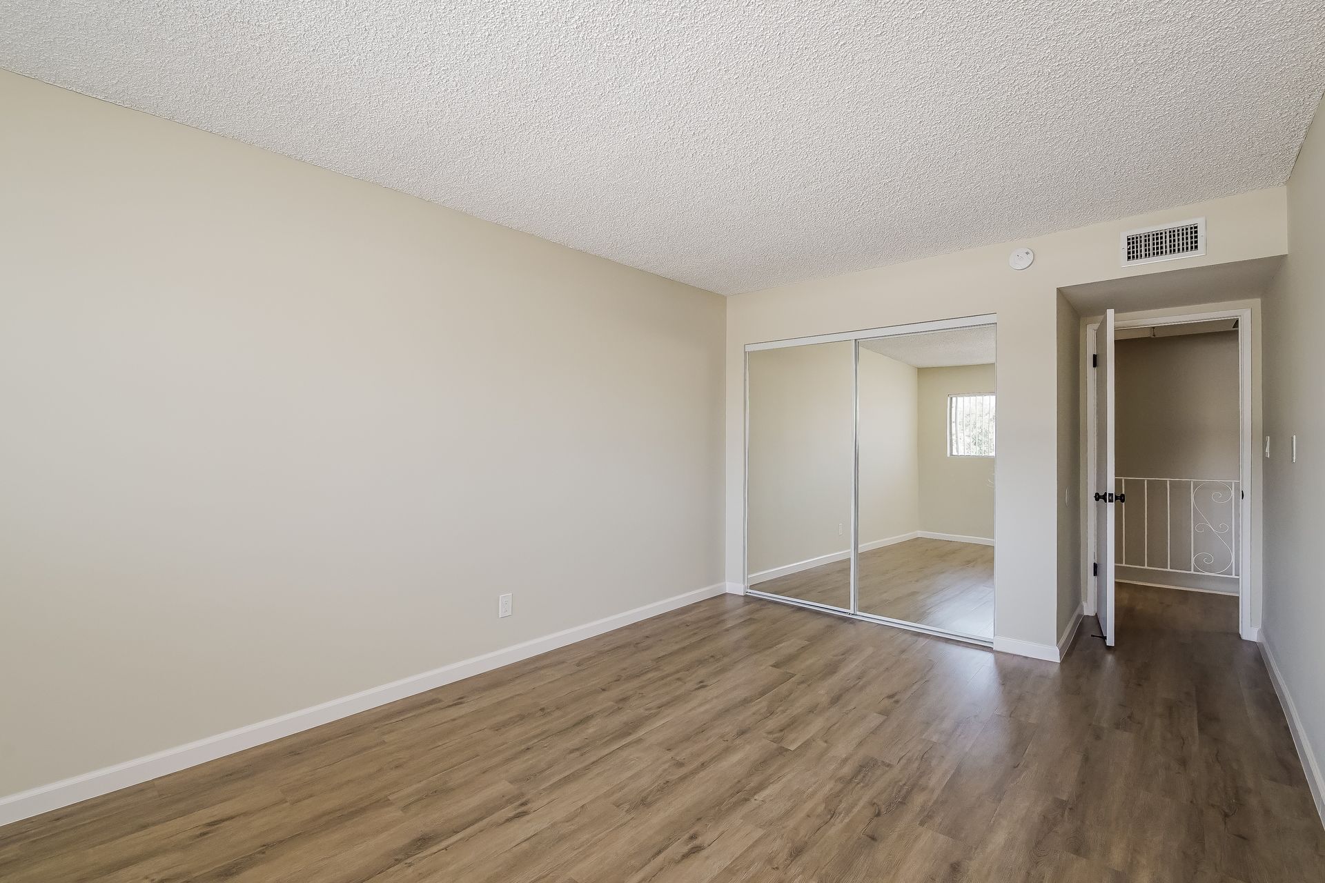 An empty living room with hardwood floors and a large mirrored closet.