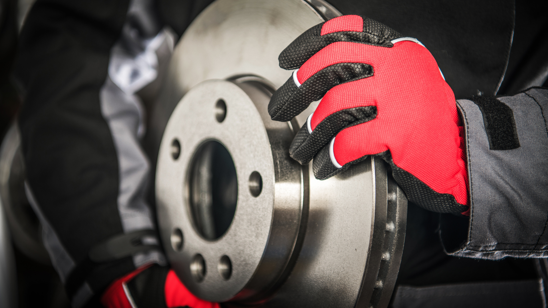 Person in red gloves holding a car brake rotor.
