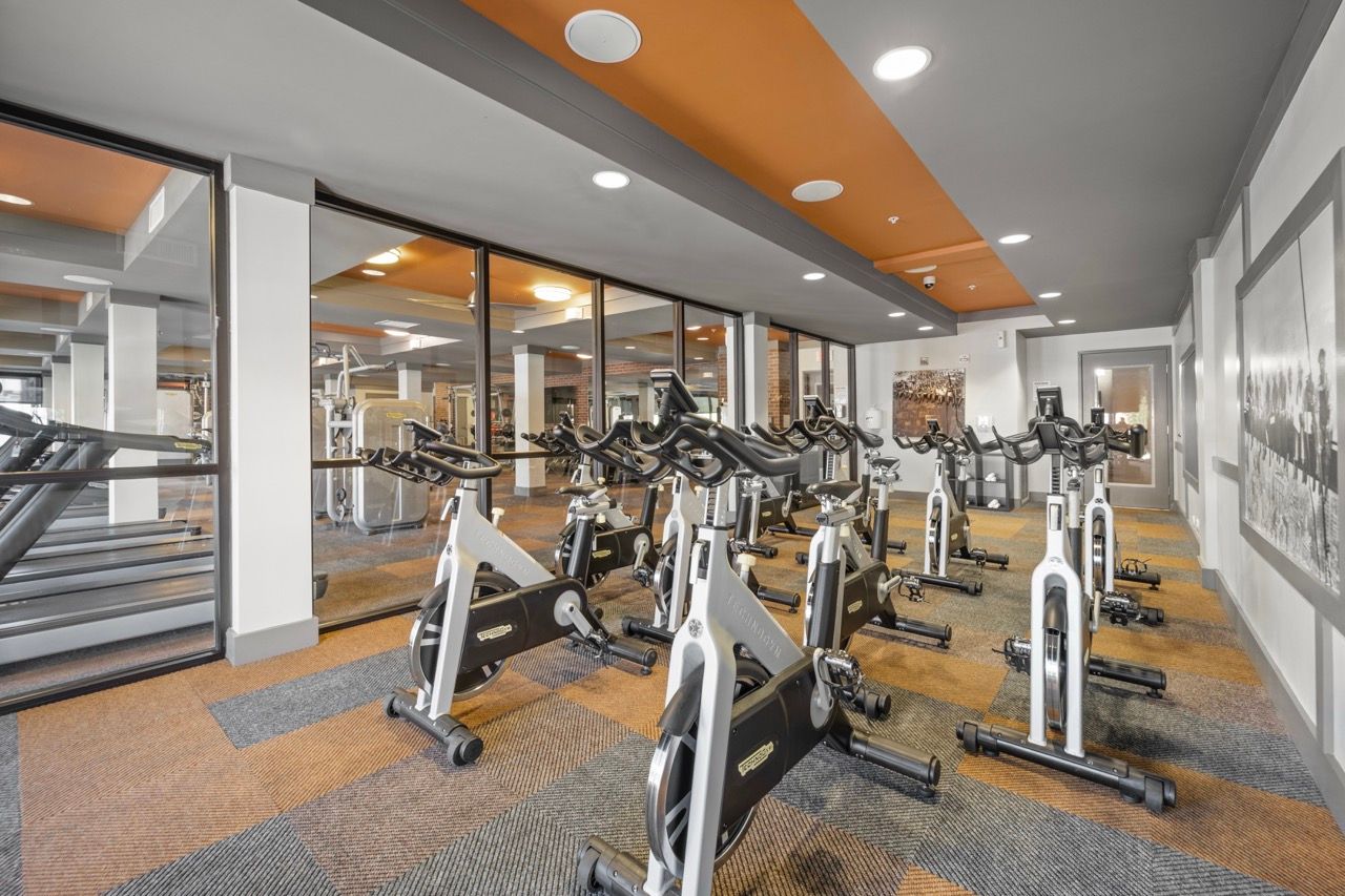 Indoor gym with rows of stationary exercise bikes and glass partitions.