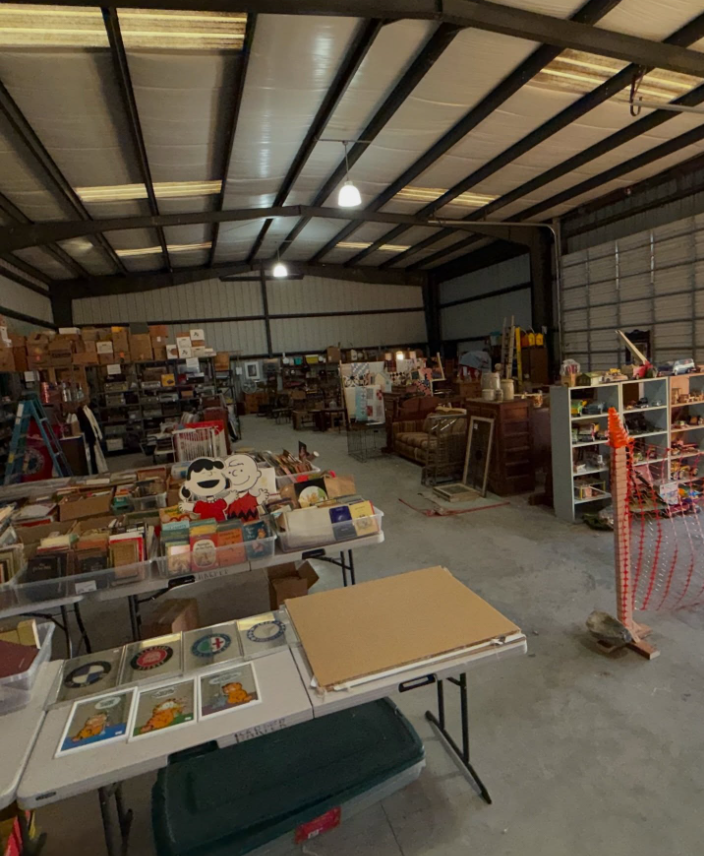 A large, open-plan indoor flea market or thrift store with tables displaying assorted goods, books, and vintage items.