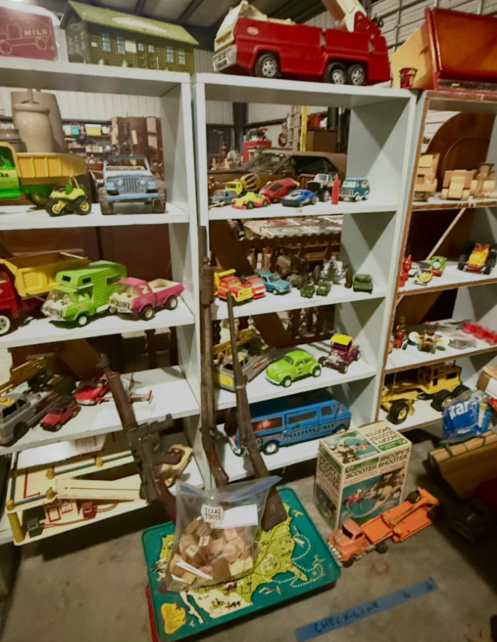 Shelves filled with various vintage metal toy vehicles, including trucks, cars, and fire engines in a storage area.