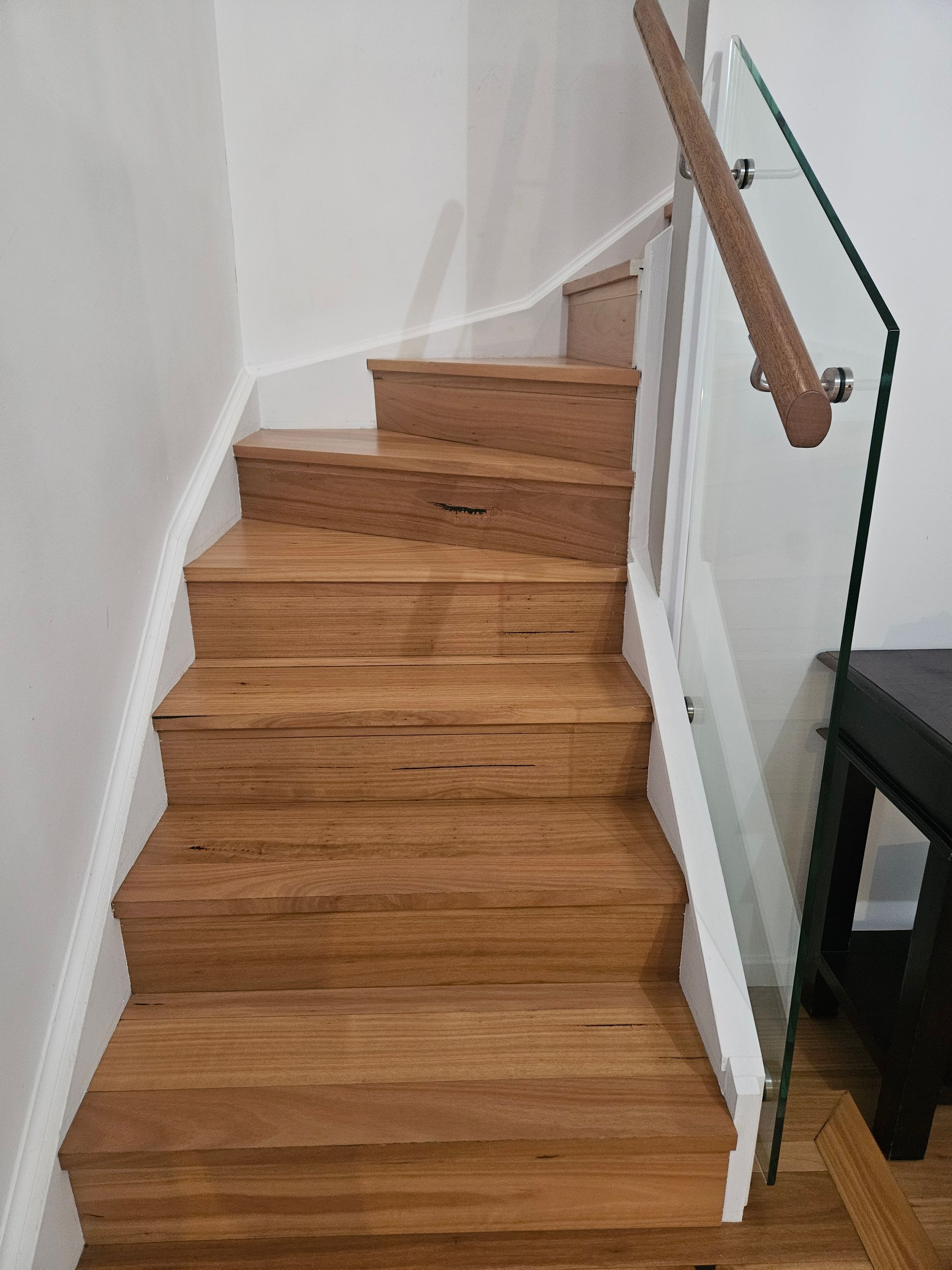 Wooden staircase with a handrail beside a glass railing in a modern interior