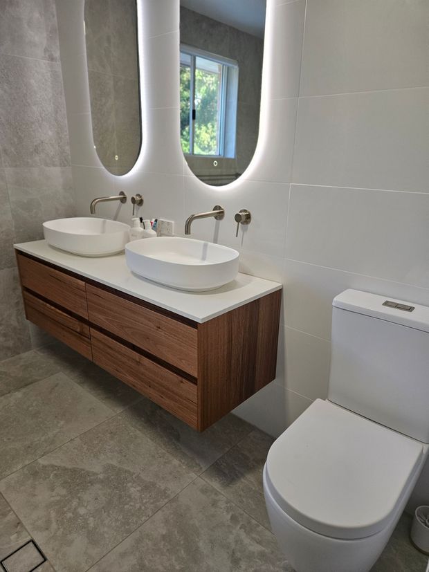 Modern bathroom with floating wood vanity, double sinks, mirror, and white toilet on gray tile floor