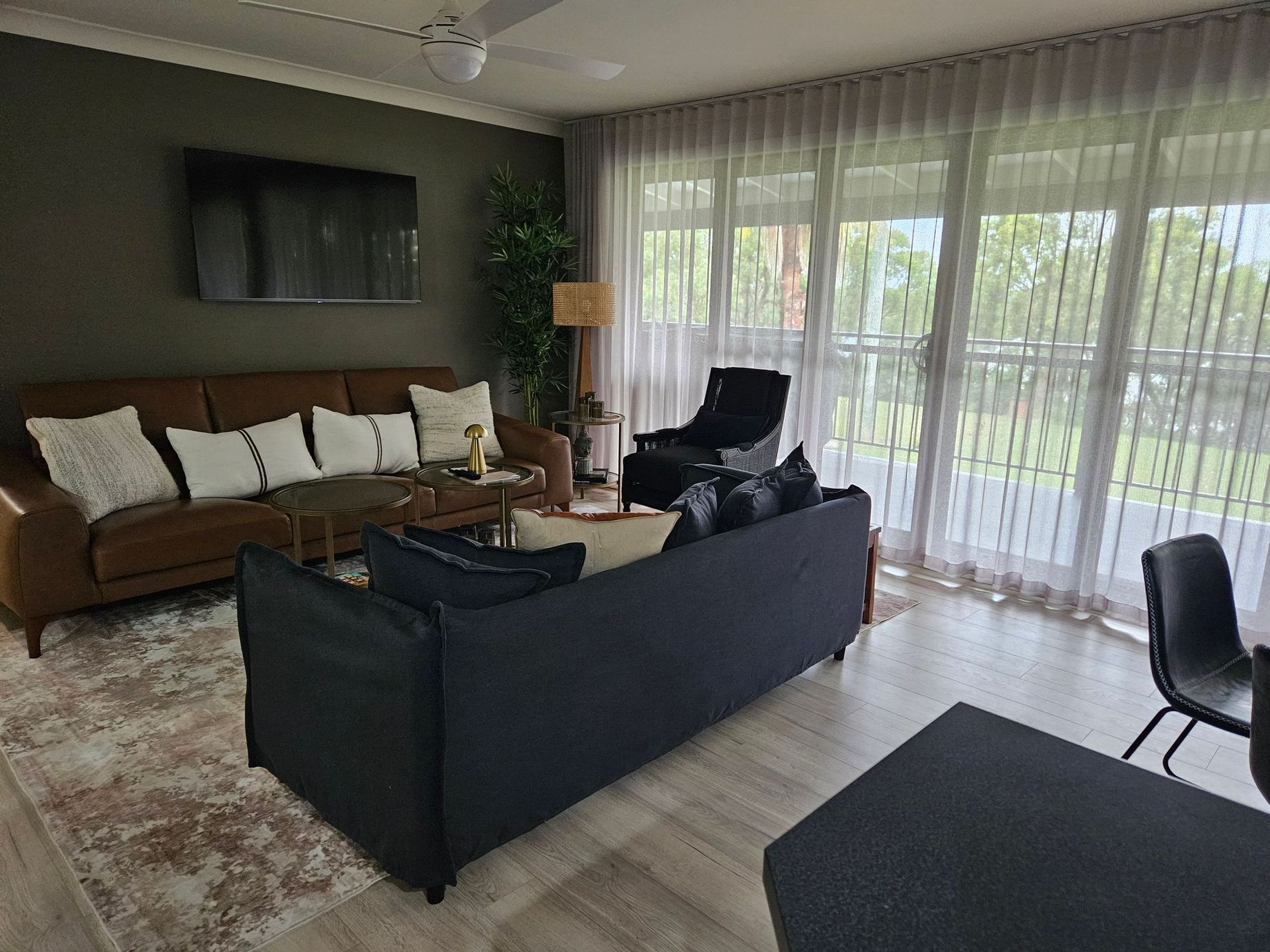 Modern living room with brown and black sofas, rug, chairs, and large windows opening to a garden.