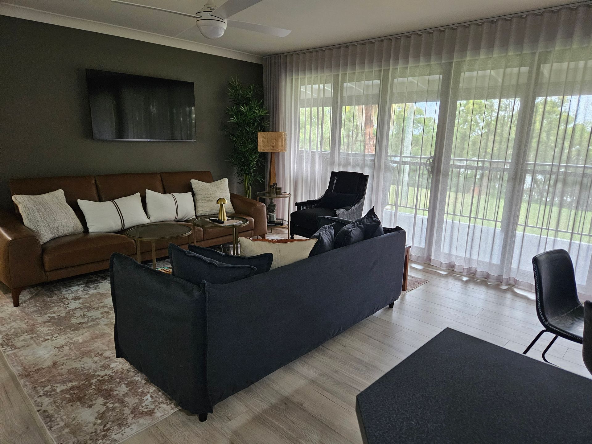 Modern living room with brown and black sofas, rug, chairs, and large windows opening to a garden.