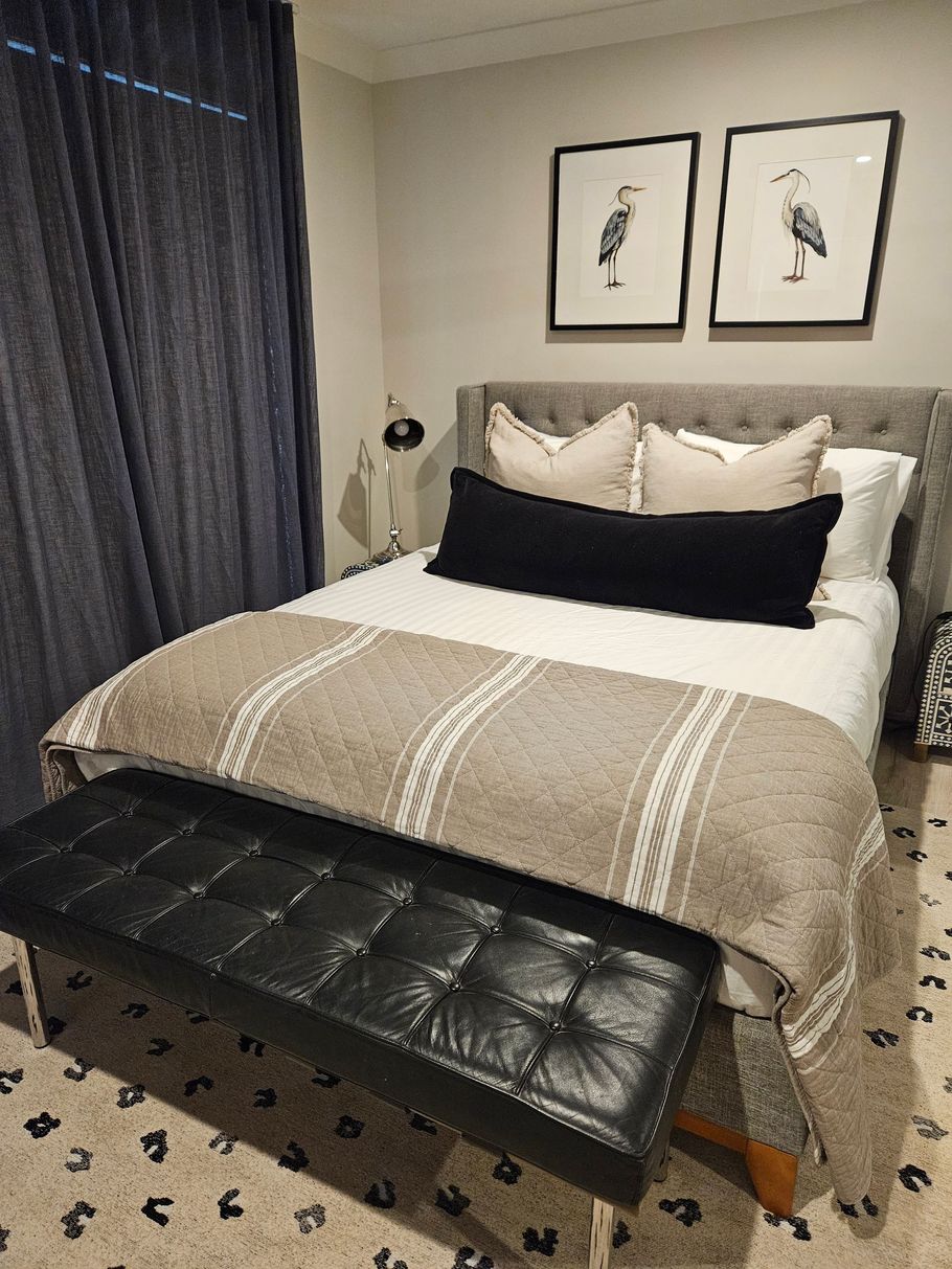 Cozy bedroom with a neatly made bed, black bench, framed art, and dark curtains.
