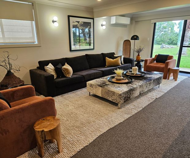 Modern living room with black sofa, patterned rug, coffee table, and large windows overlooking greenery