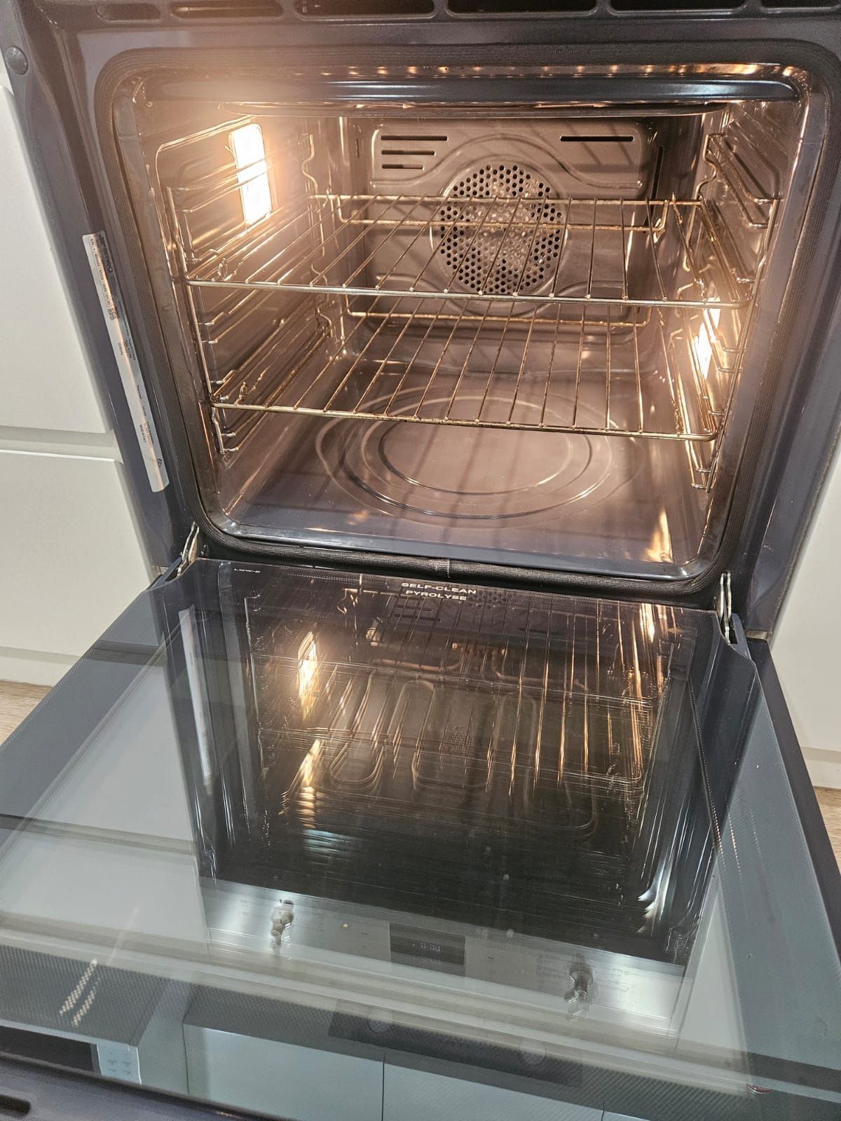 Open oven with warm interior light and metal racks, door hinged downward.