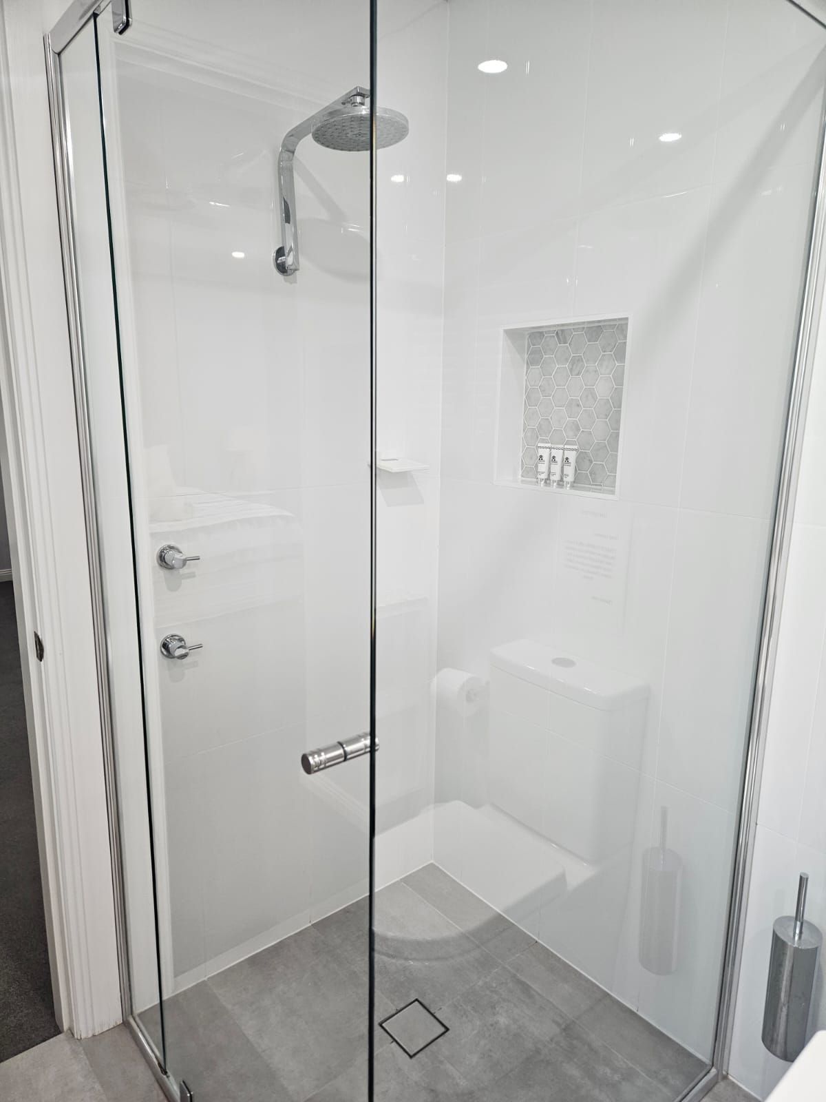 Glass shower enclosure in a white bathroom with a chrome showerhead and gray tile floor.