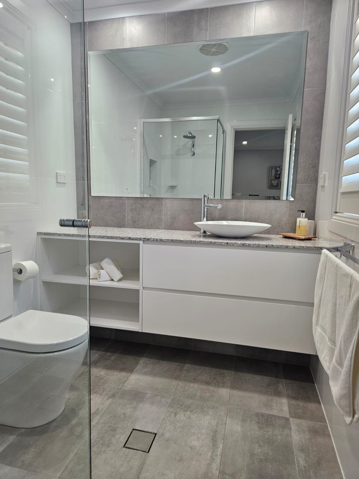 Modern bathroom with gray tile, large mirror, white vanity, toilet, and wall-mounted sink.