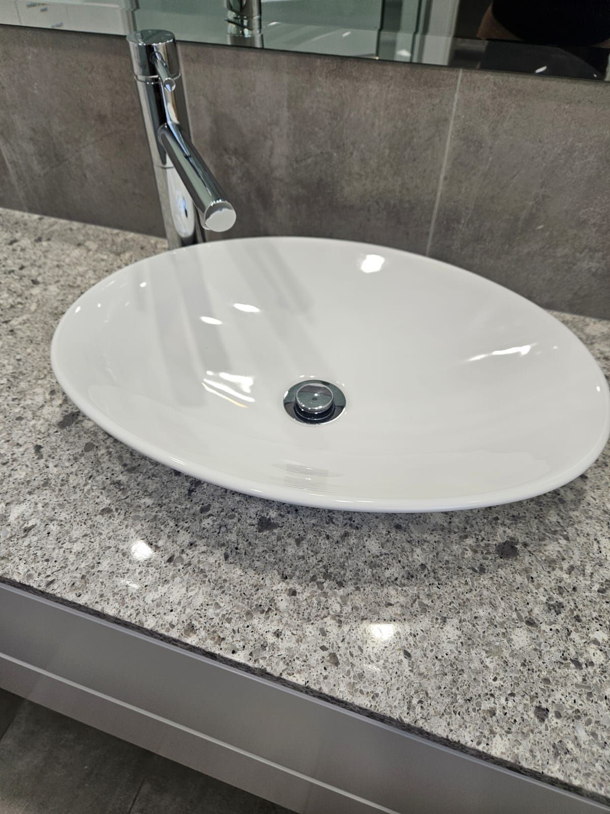 White oval bathroom sink on granite countertop with chrome faucet