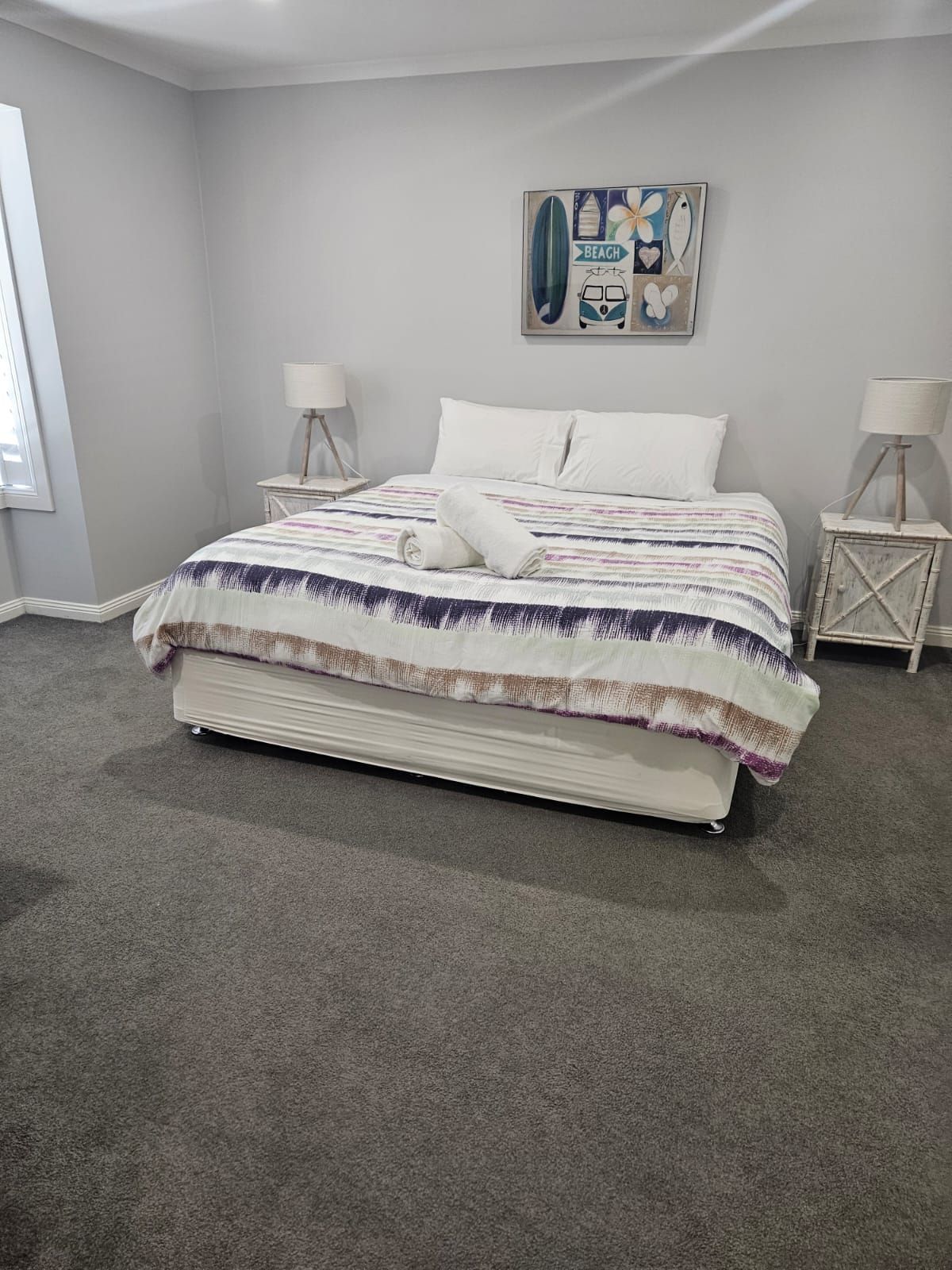 Bright gray bedroom with a white bed, matching side tables, lamps, and a framed wall art piece.