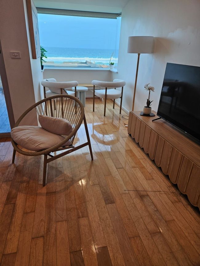 Bright living room with wicker chair, TV, and ocean view through open doorway