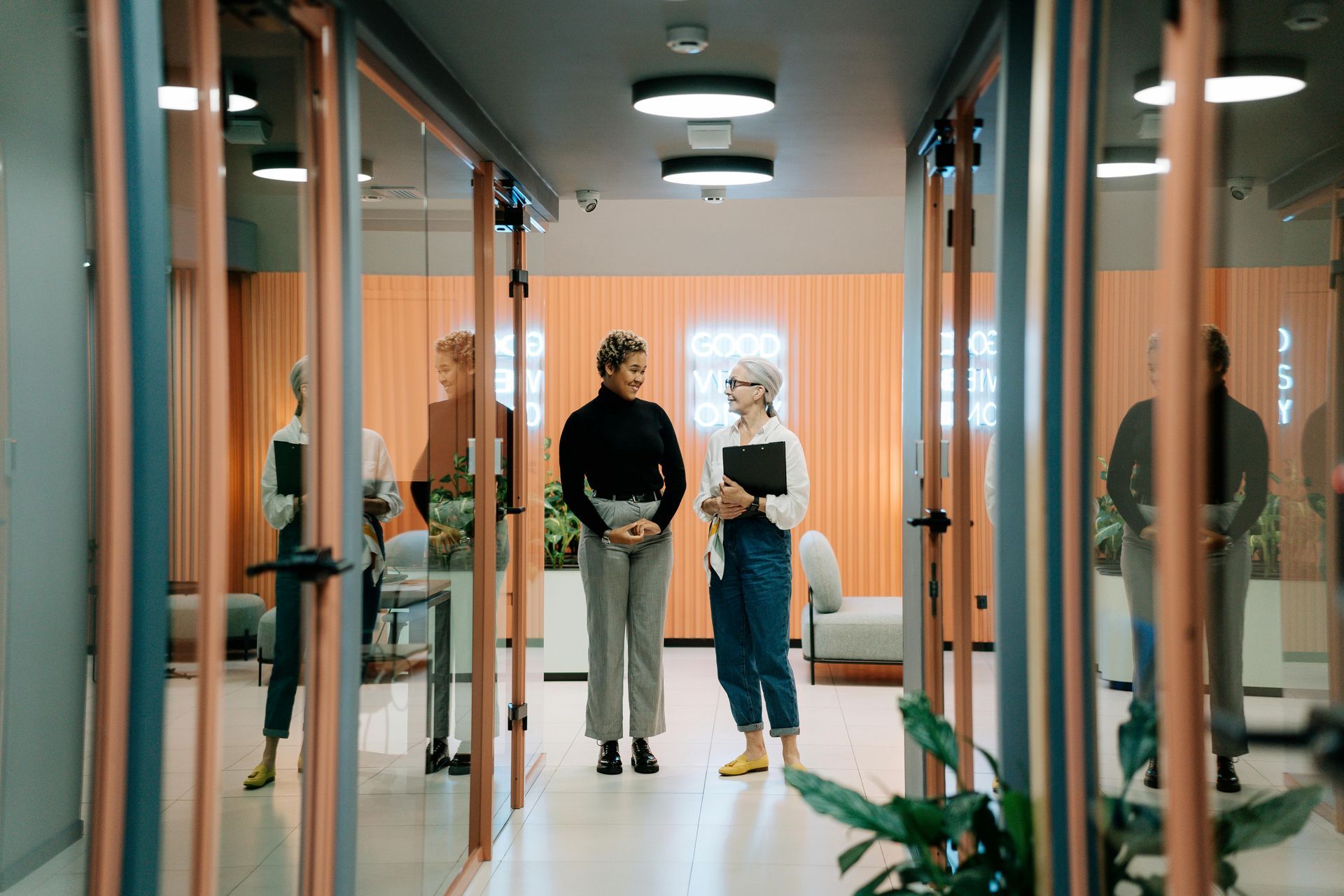 Two women are standing in a hallway talking to each other at work.