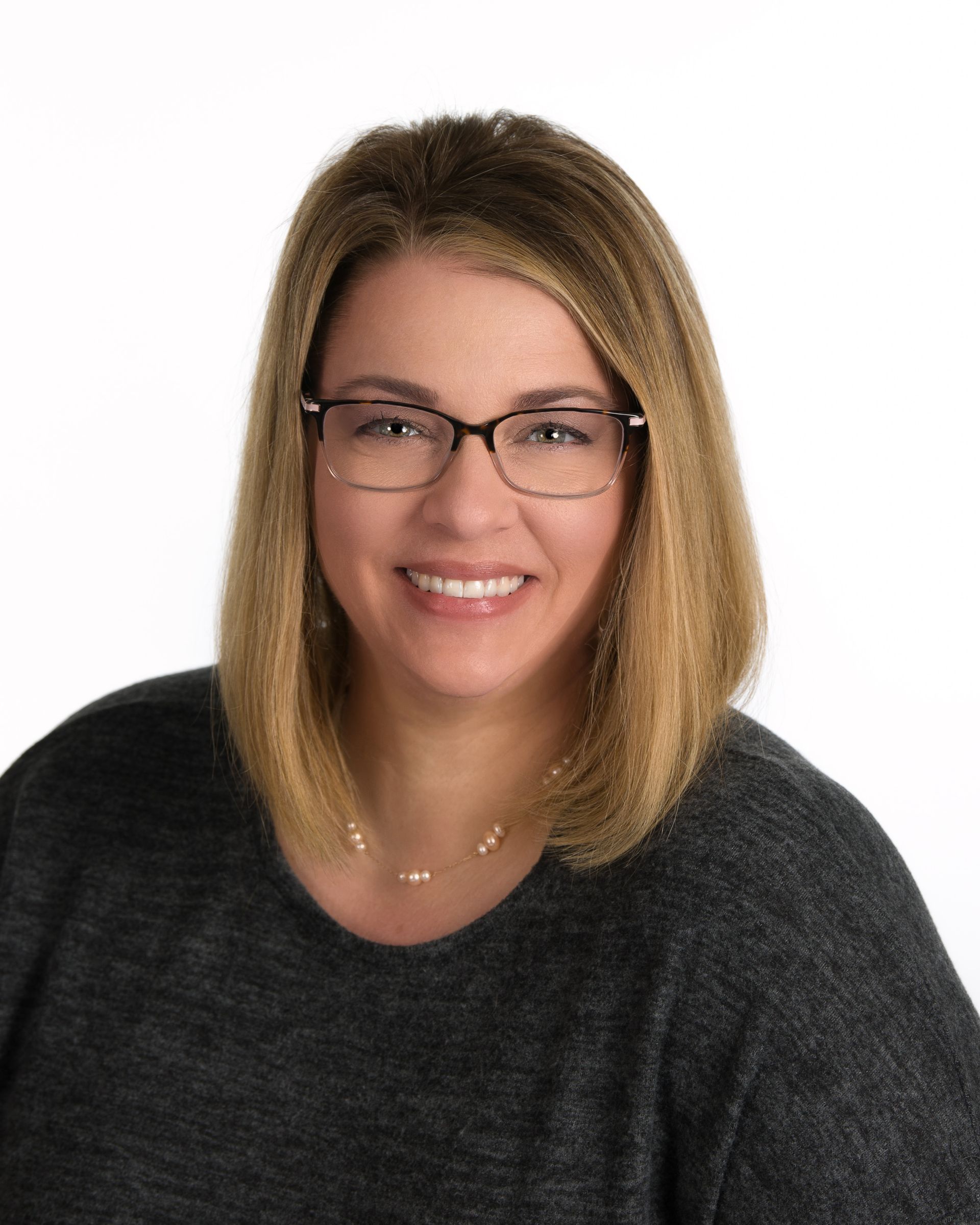 Woman with glasses smiling in a dark sweater against a white background