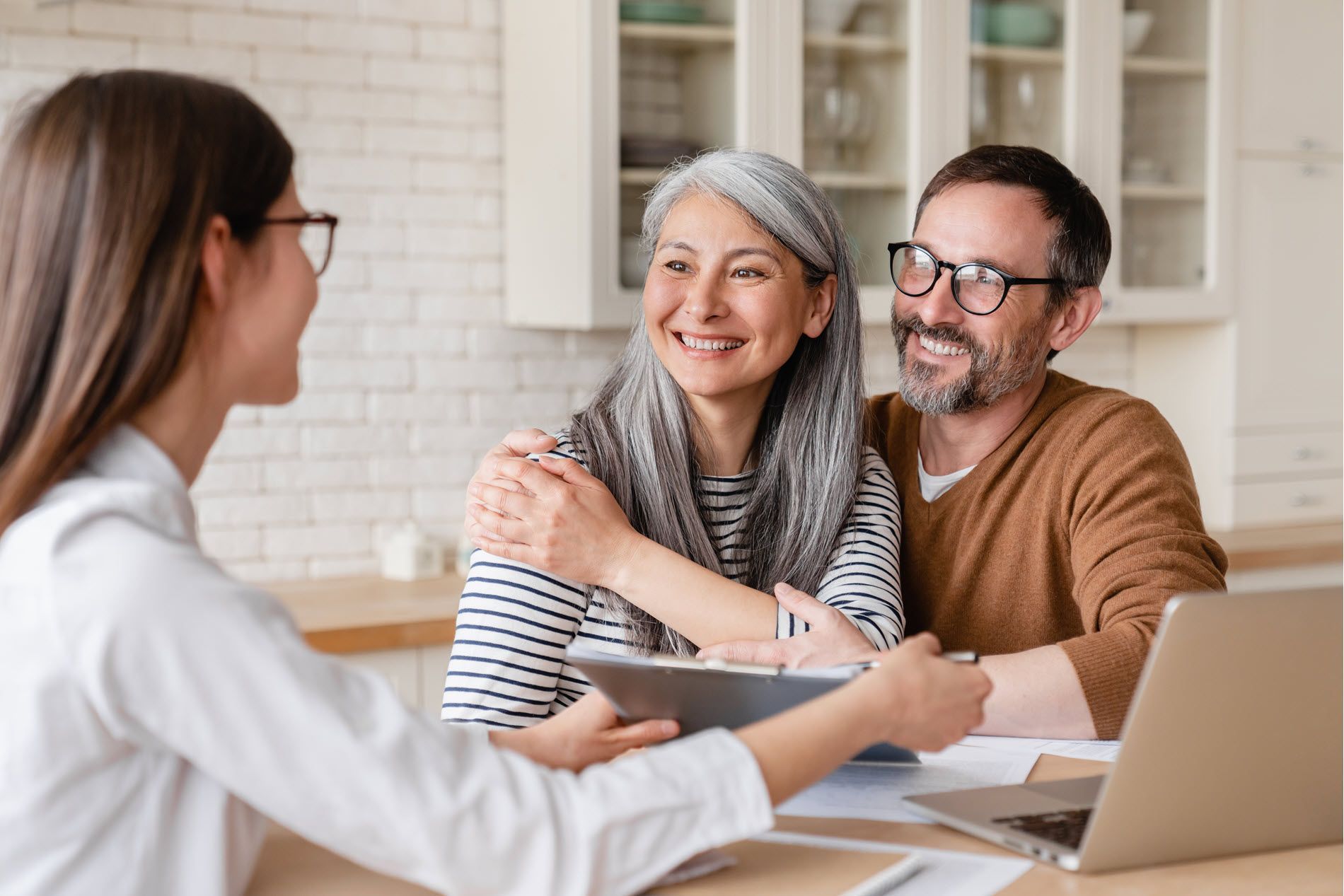Consultation in a bright office: a smiling couple meets with a woman across a table, laptop open.