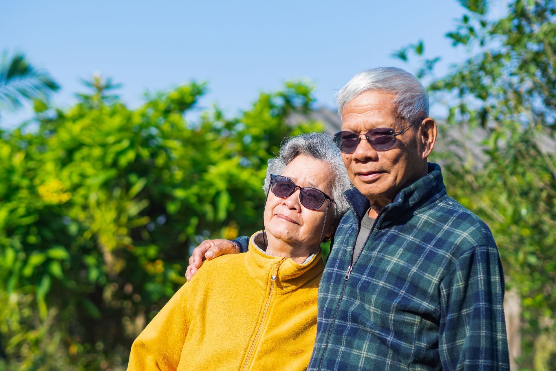 Two smiling people outdoors, wearing sunglasses and standing against a bright green background