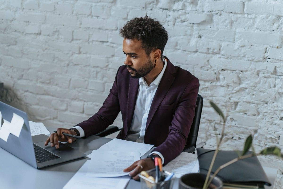 Person working on a laptop at a desk with a notebook and lamp