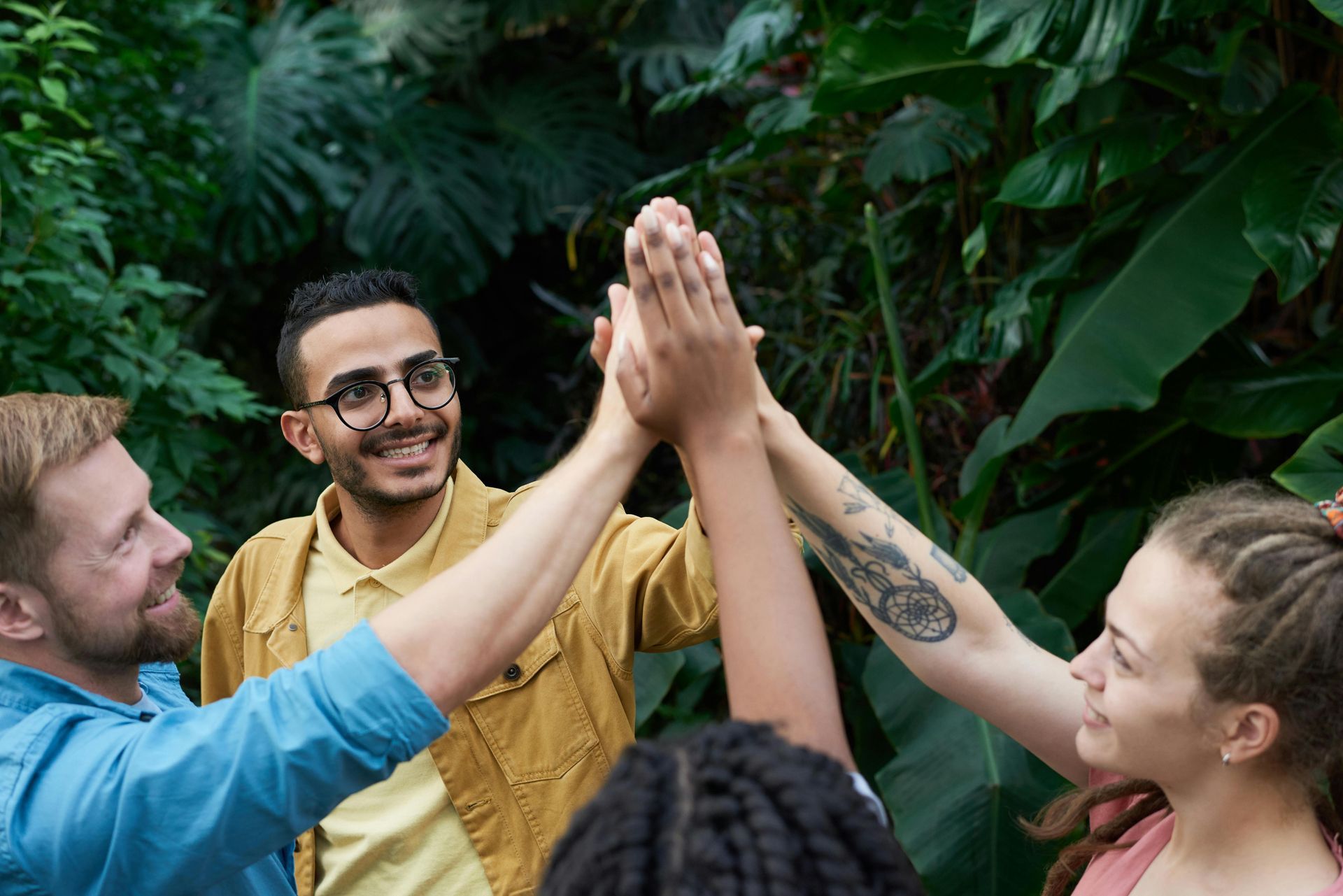 Three people high-five in a lush green garden, smiling and celebrating.
