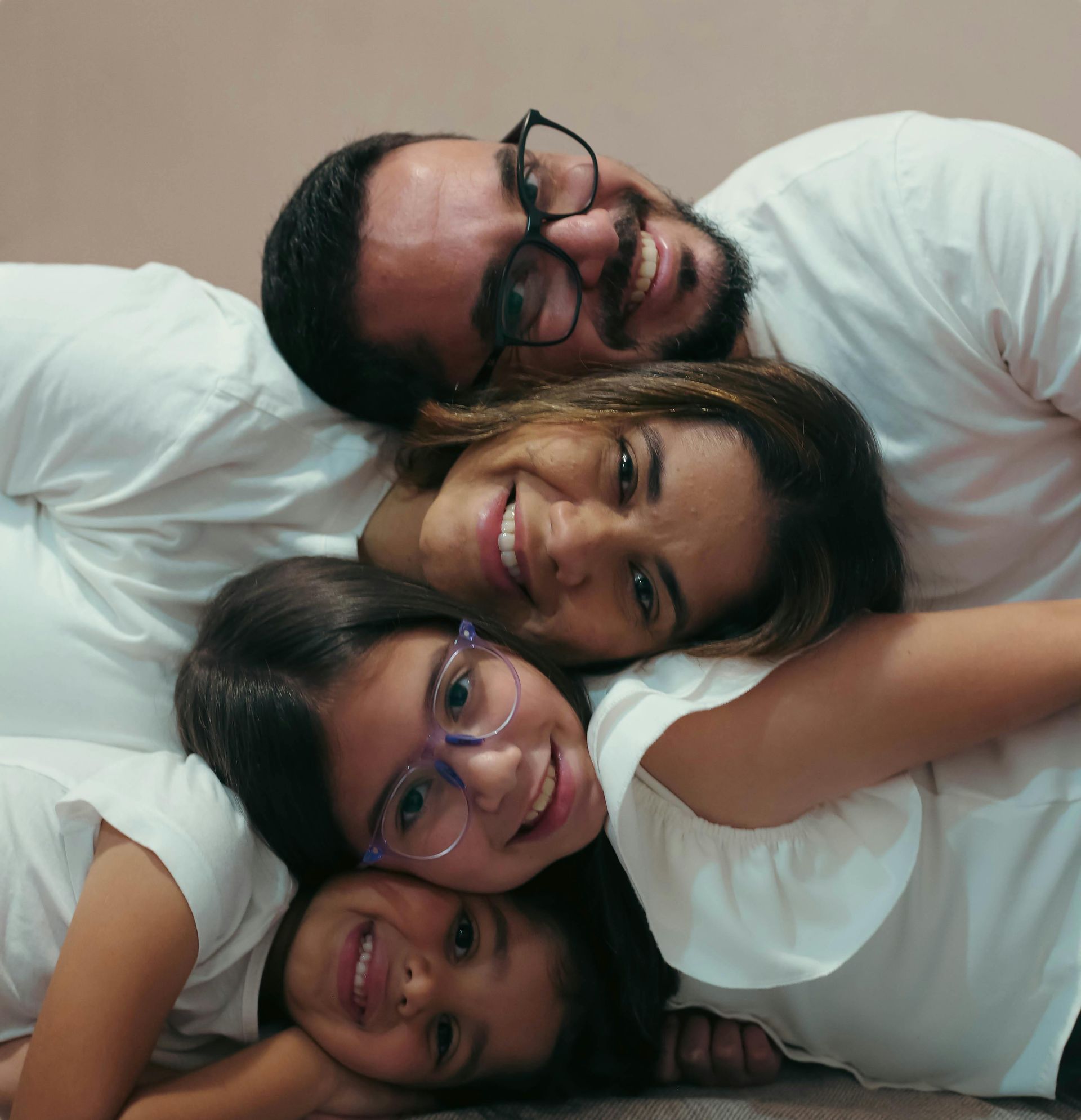 Four smiling people piled together in white shirts, posing closely on a couch.