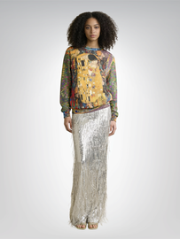Woman in a sweater printed with a painting, and a long silver sequined skirt.